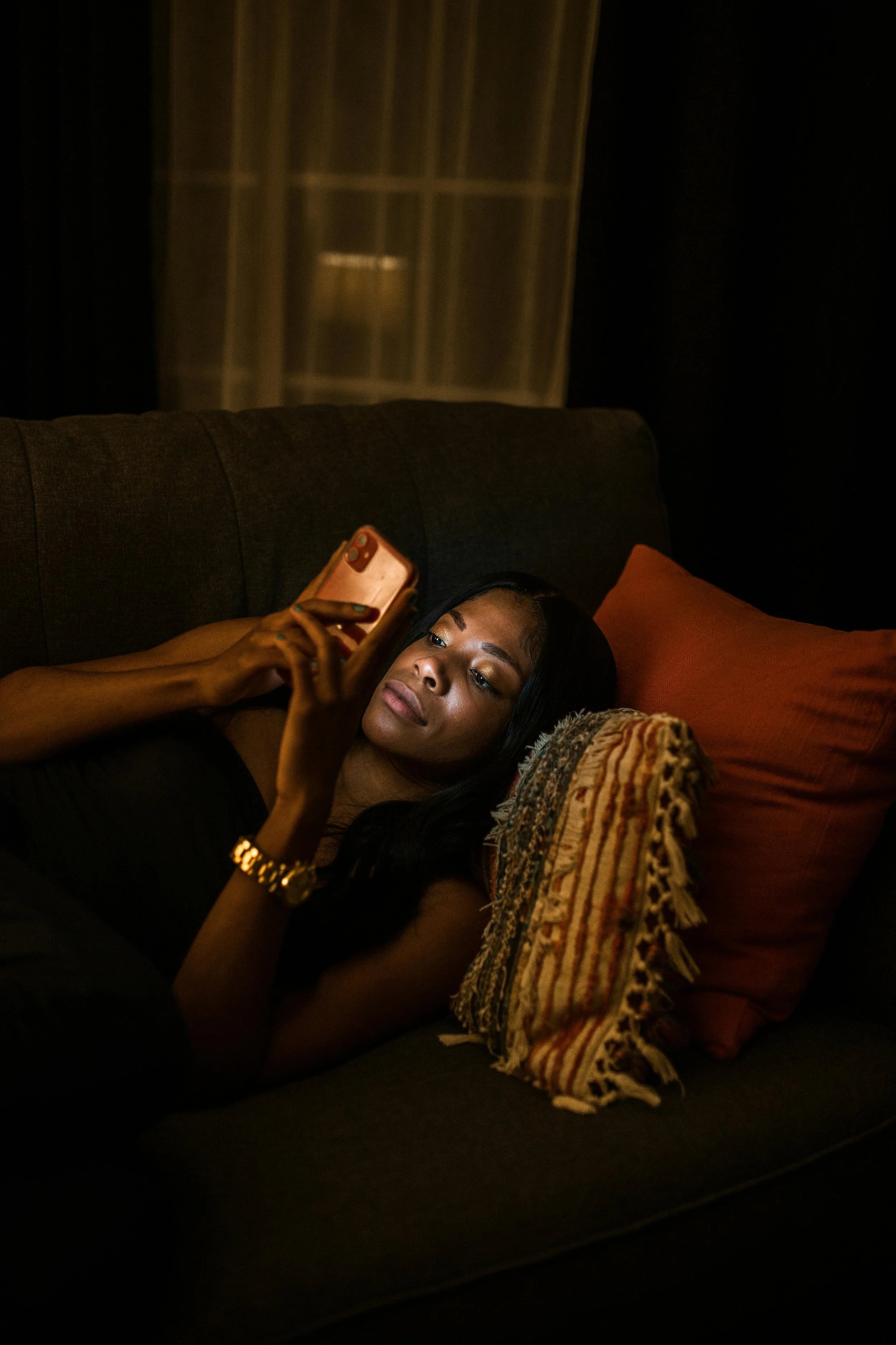 Woman lying on a couch in low light, looking at her phone, reflecting how the body holds emotional memory in family estrangement.