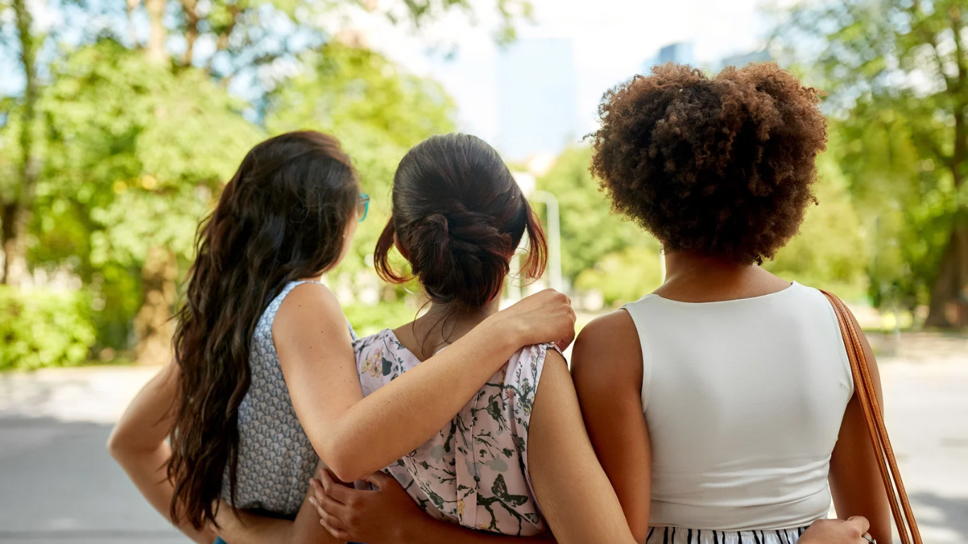 A diverse group of three women standing arm-in-arm, looking into the distance, symbolizing unity, support, and the strength of secure friendships.