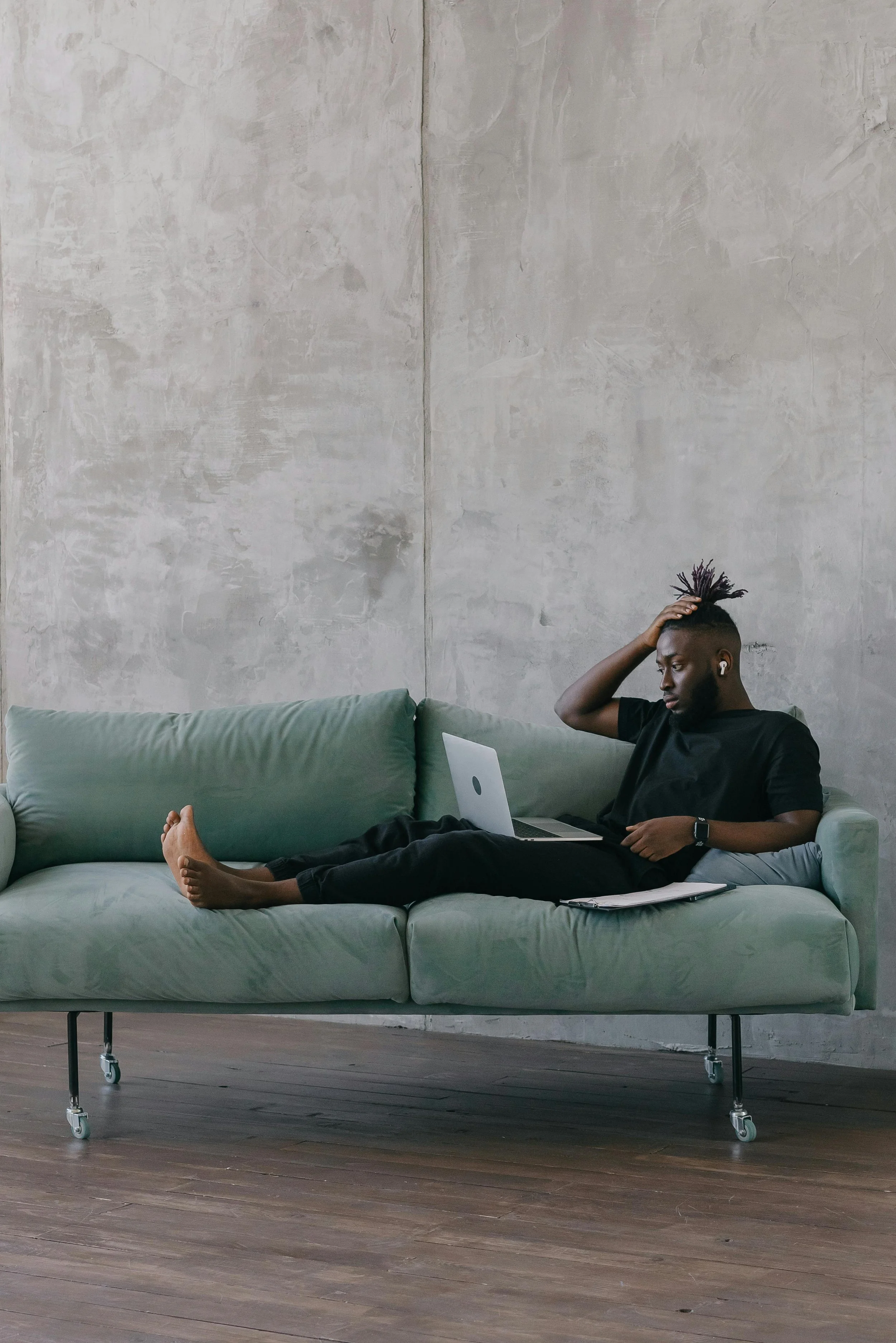 Man sitting alone on a couch with a laptop, conveying quiet solitude and the weight of carrying something privately