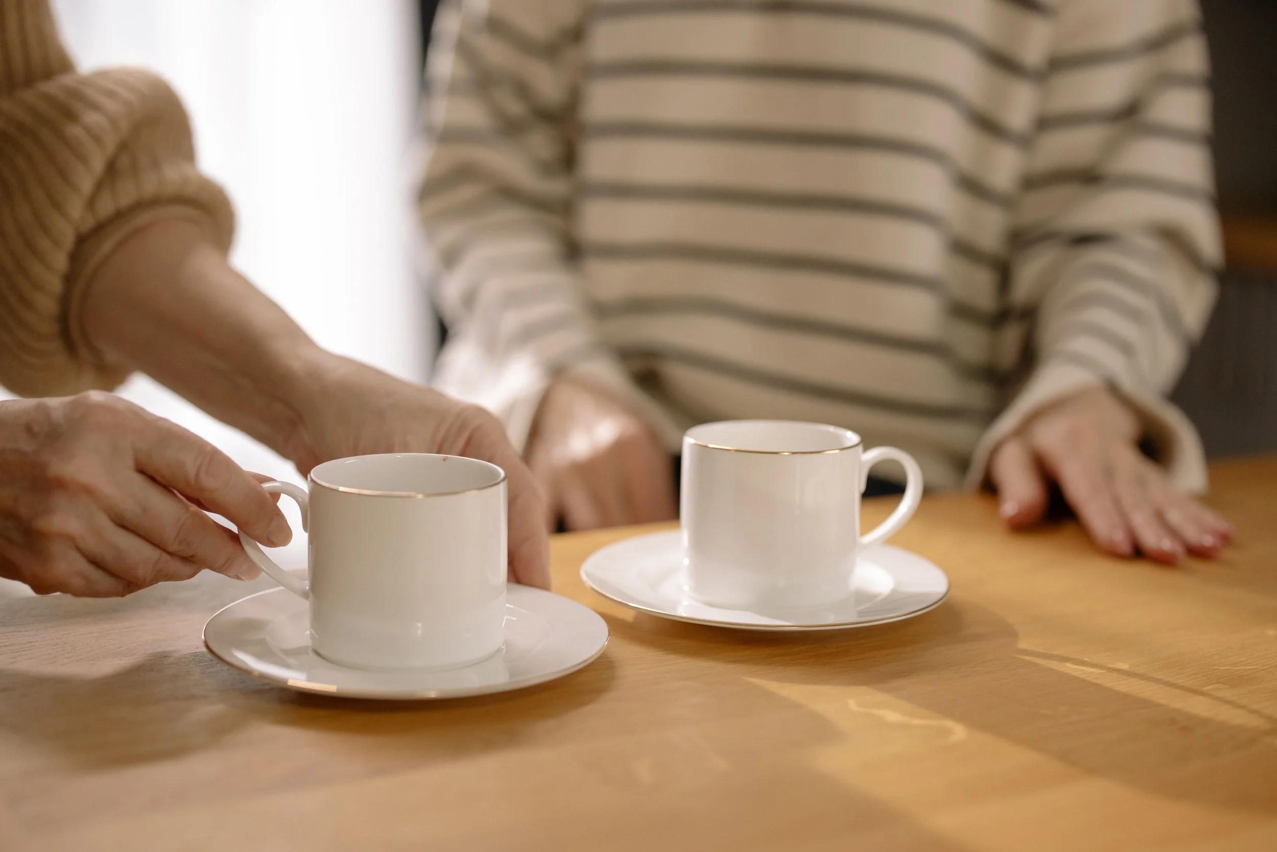 Two people talking over coffee in warm light, representing the chosen relationships that hold clients through complicated family work.