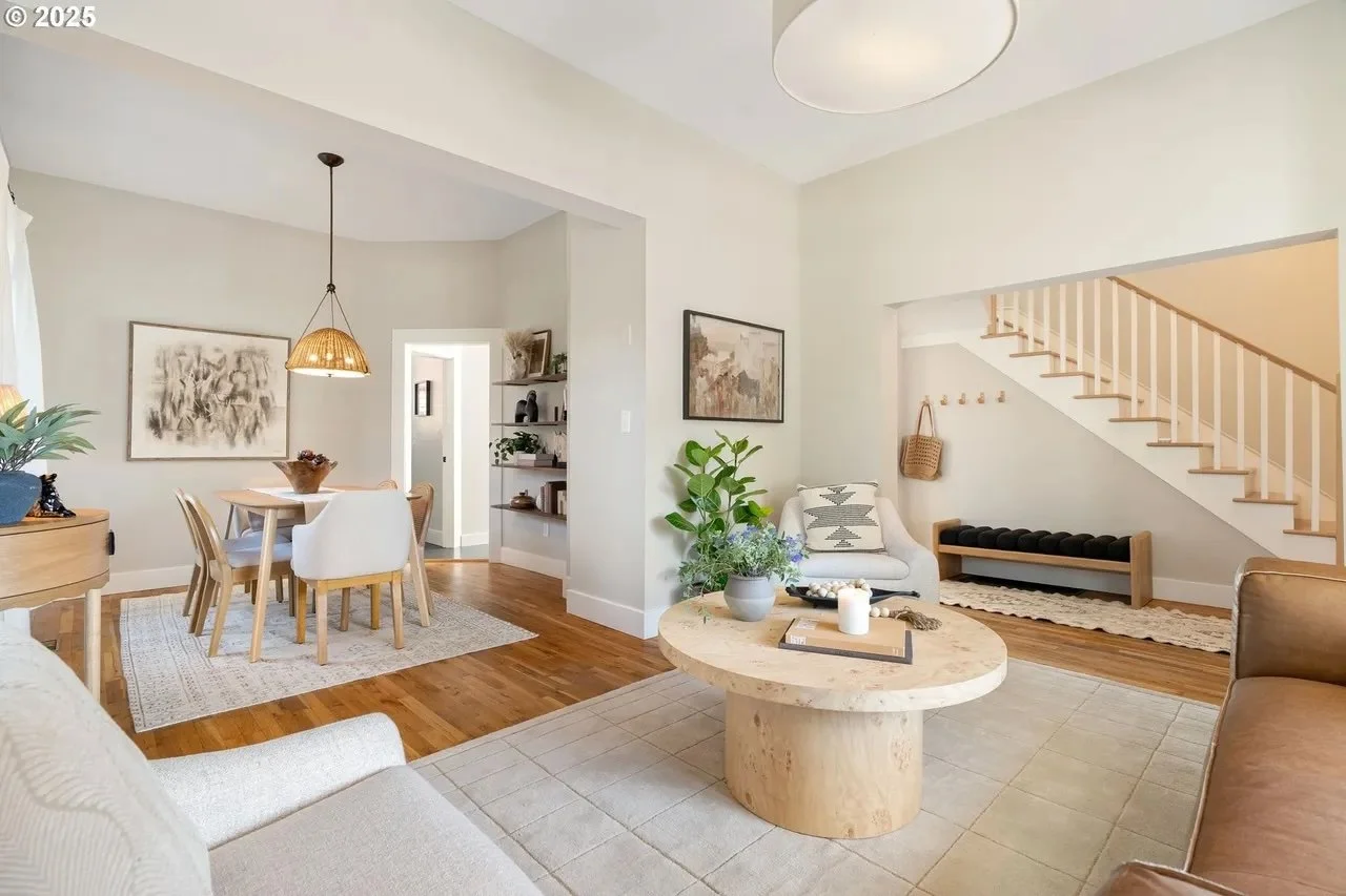 Bright open living and dining area with wooden furniture, a staircase, and decor in neutral tones.