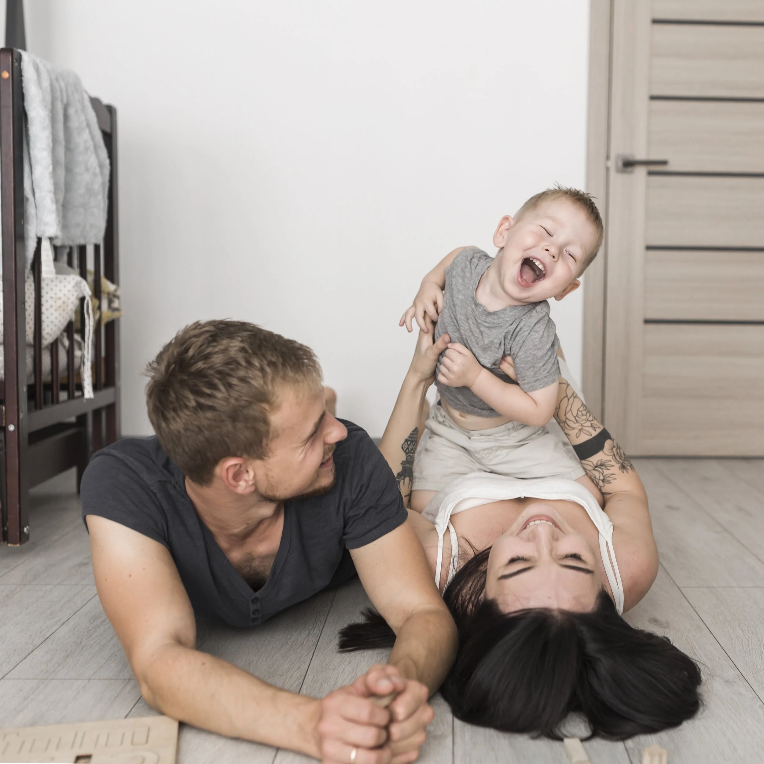 A happy family, including a father, mother, and young son, playing and laughing on the floor of a home.