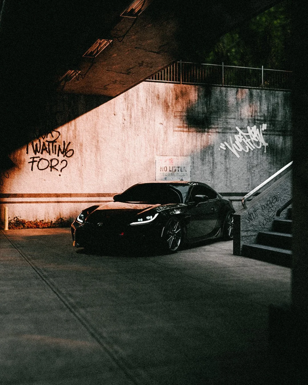 Black coupe by a stairwell wall that reads “What are you waiting for?”