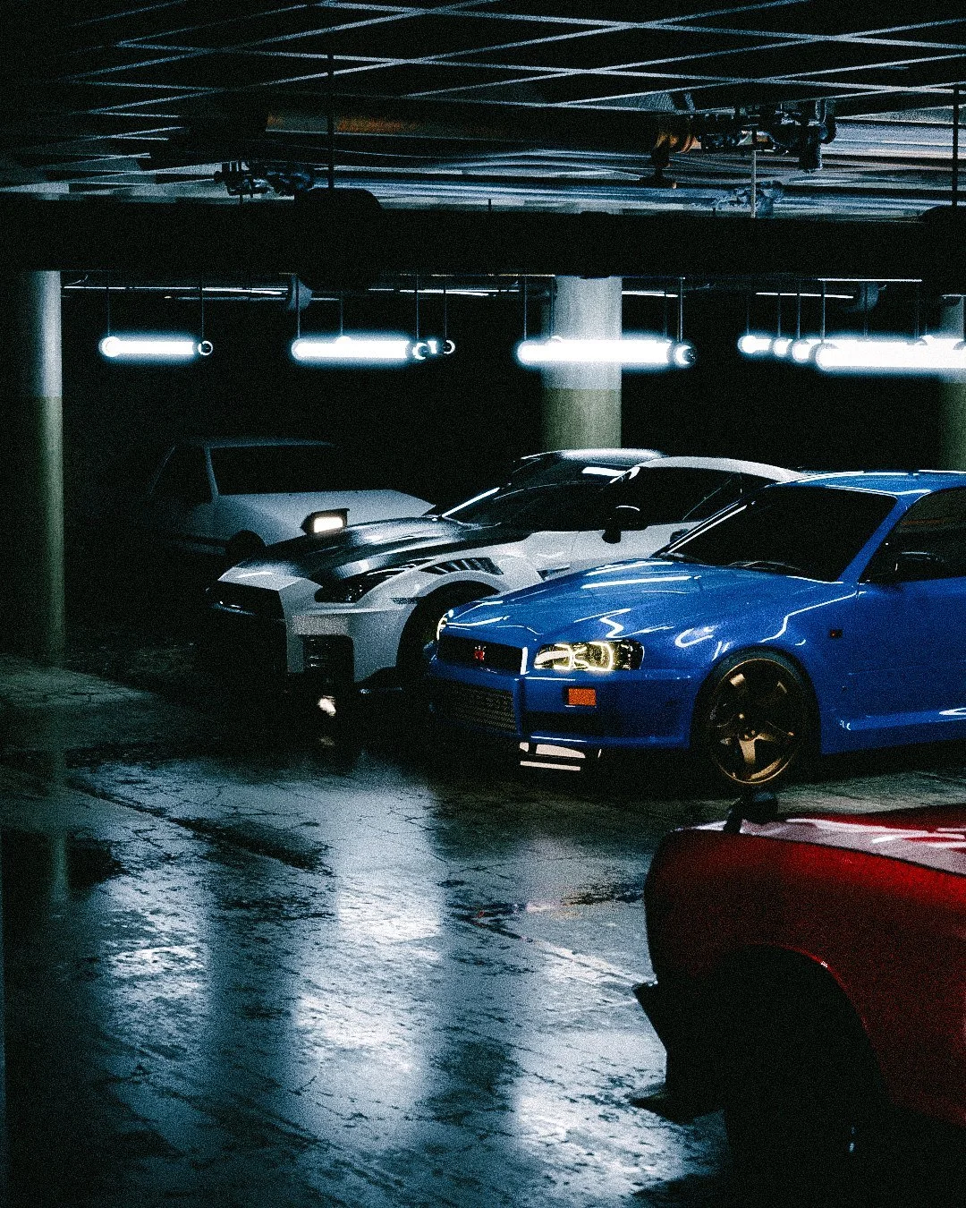 Blue Skyline and a white GT-R under rows of garage lights