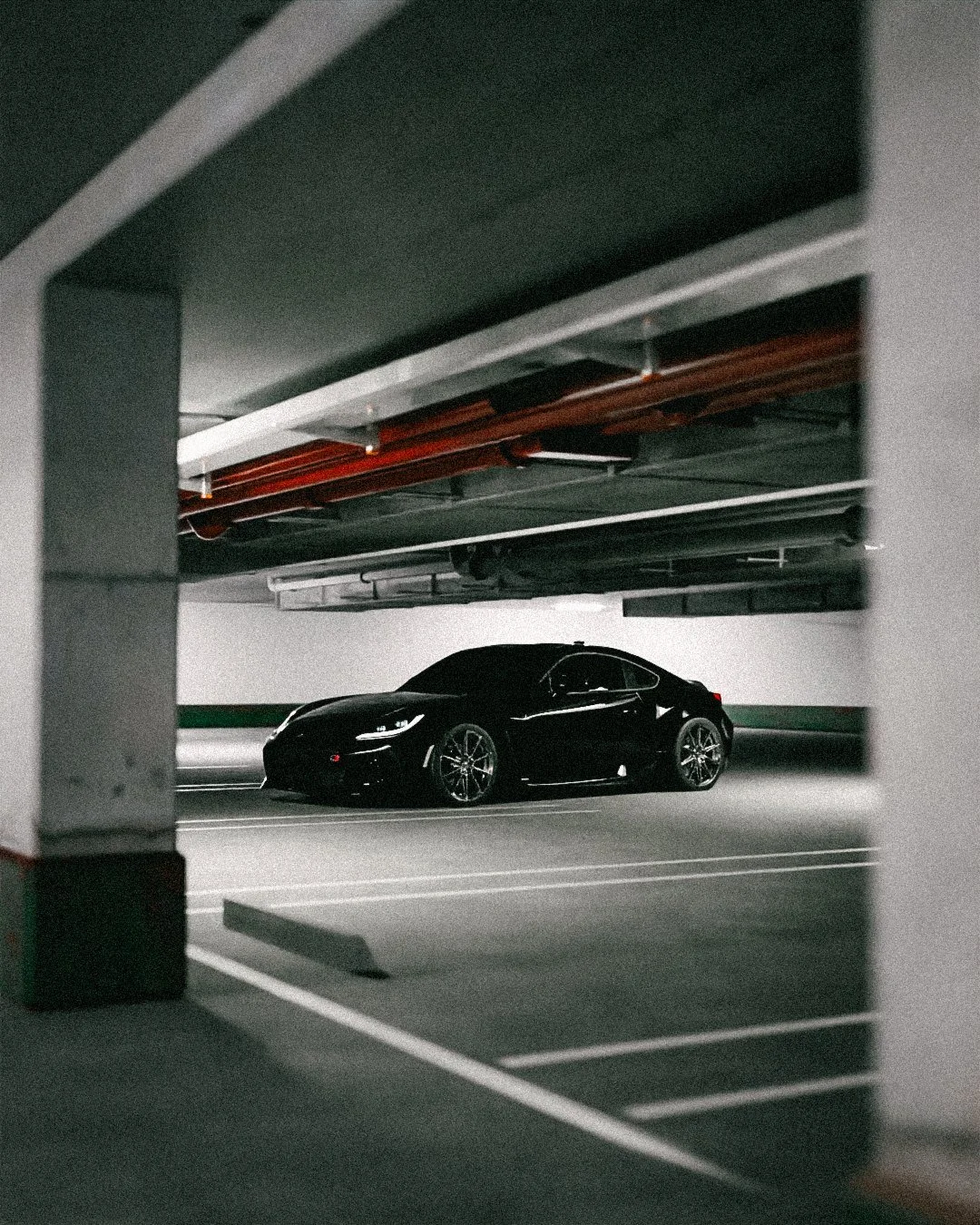 Black coupe in a white parking garage with orange beams