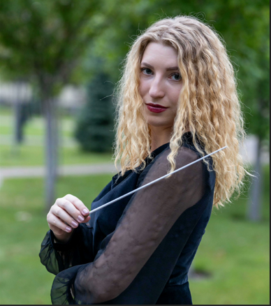 Blonde woman in a black sheer-sleeved top posing outdoors in a park