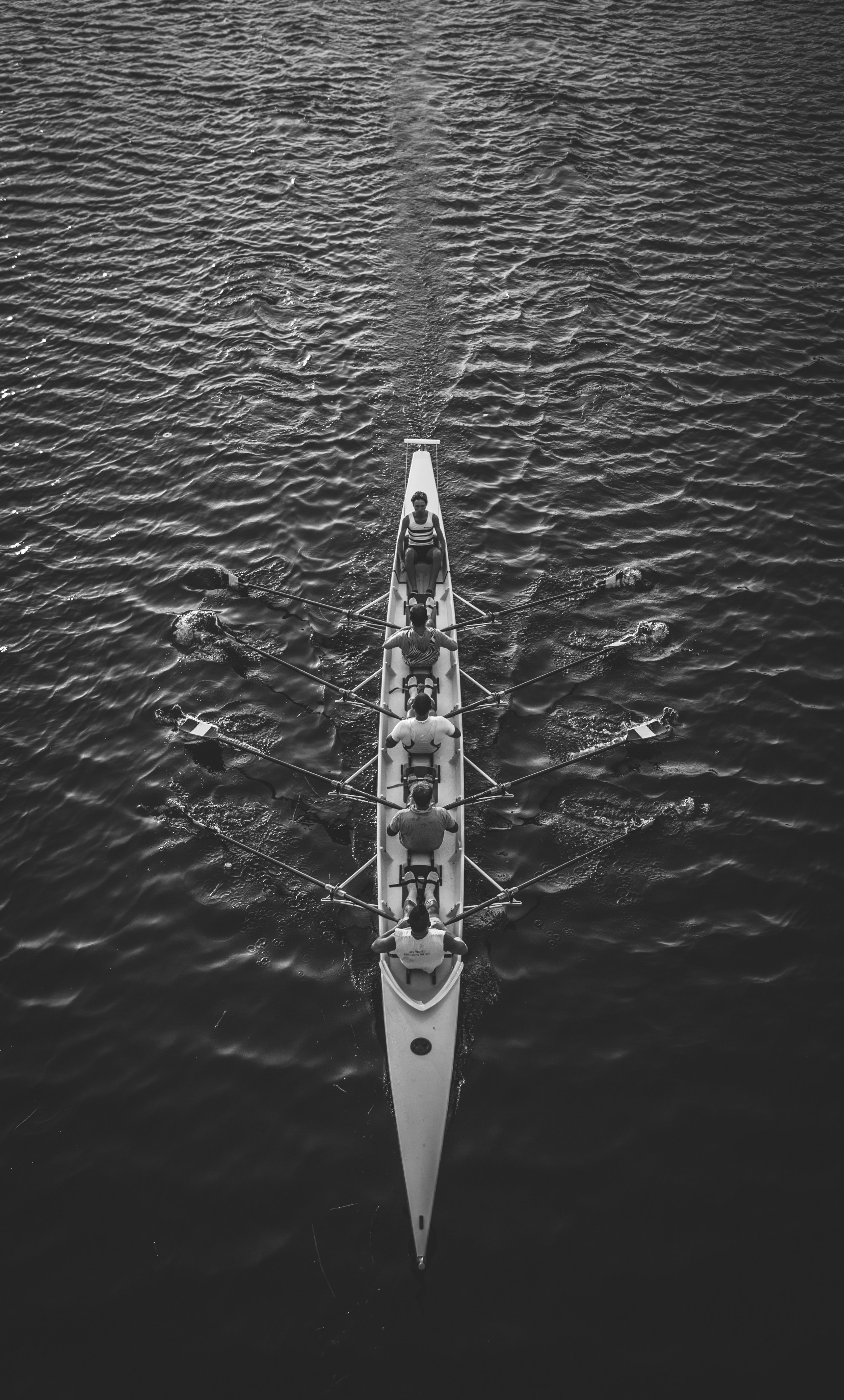Aerial view of a rowing team from above in a boat on calm water, with six rowers and a coxswain.