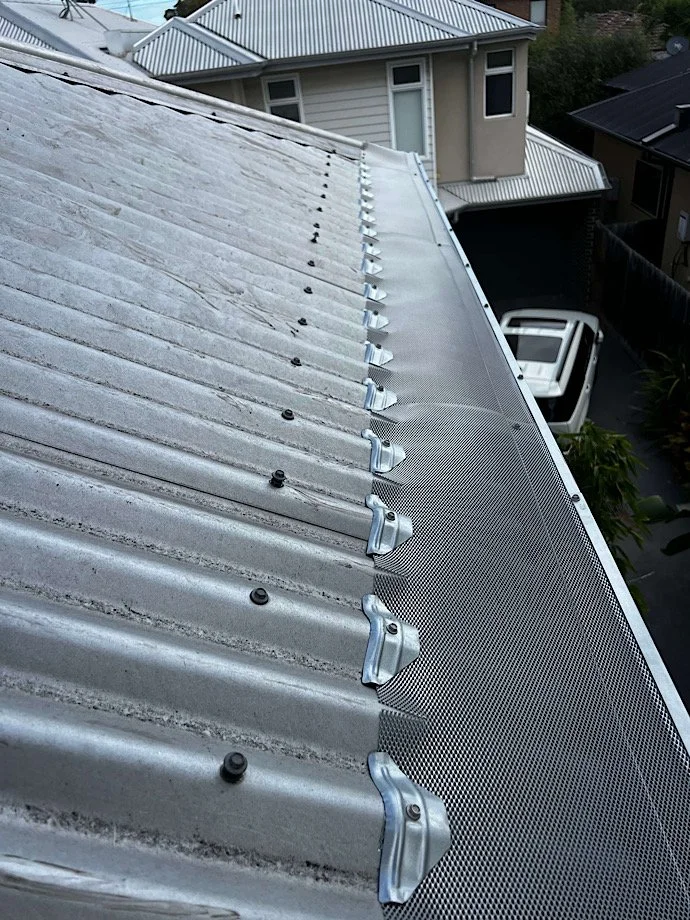 Metal roofing being installed on a building, with a ladder and a wooden fence in the background.