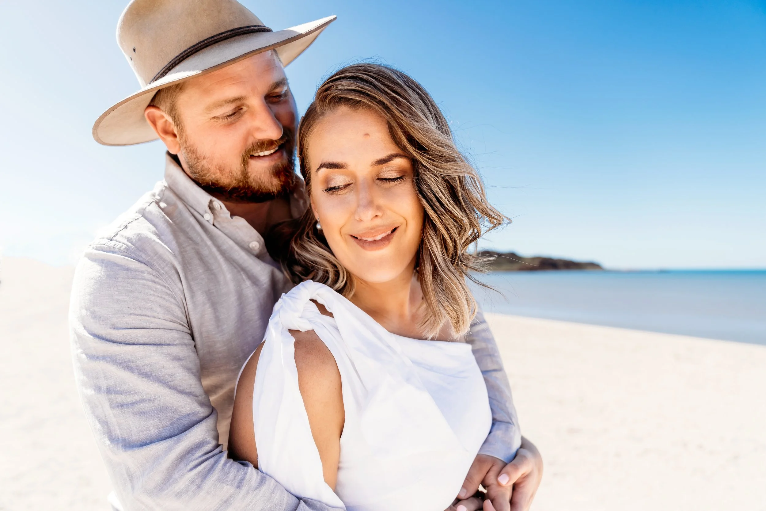 Happy couple wearing light toned linen wedding outfits after their elopement with blue water of Hearson's Cove in the background