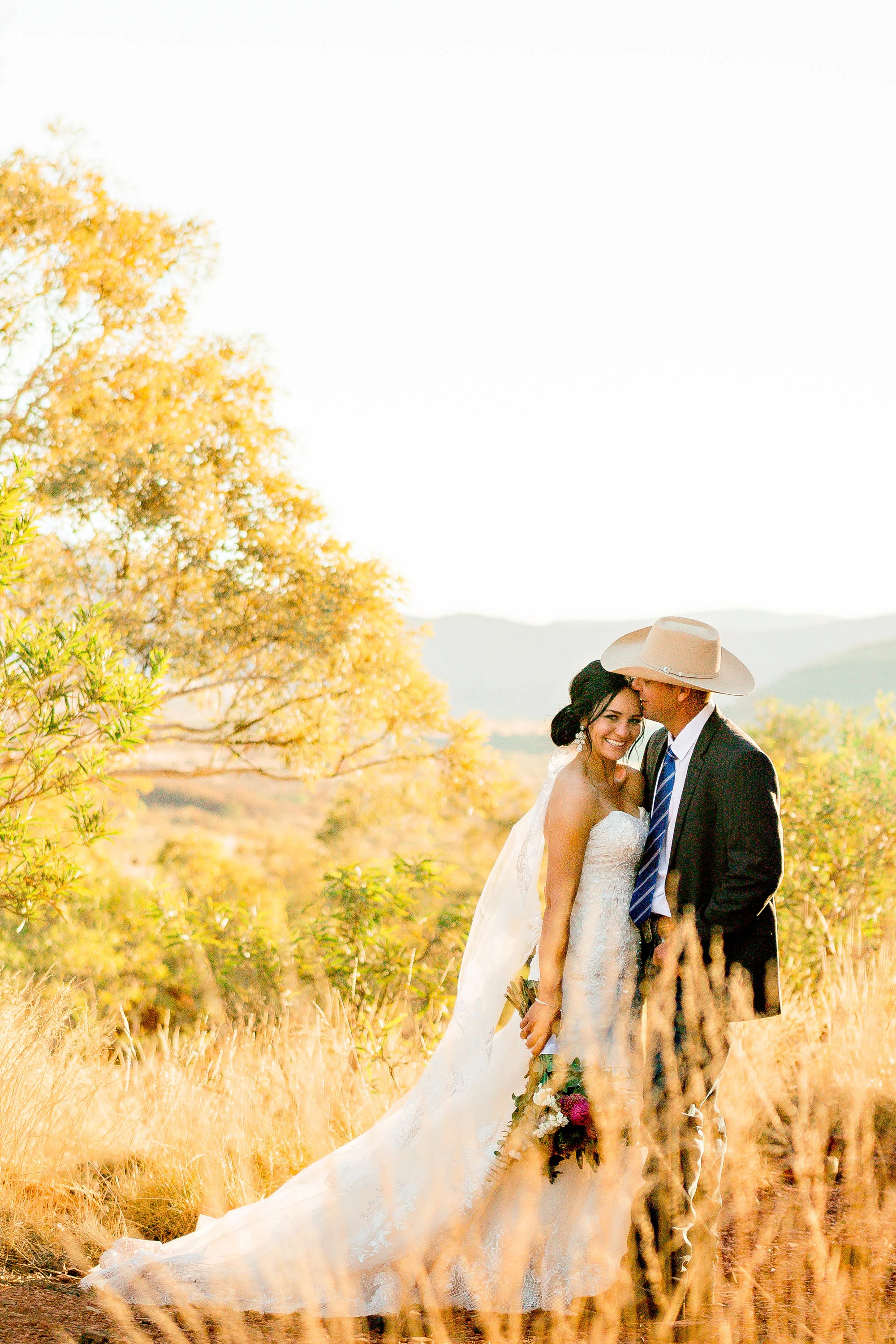 groom kissing bride on forehead as she looks towards the camera in golden outback scene
