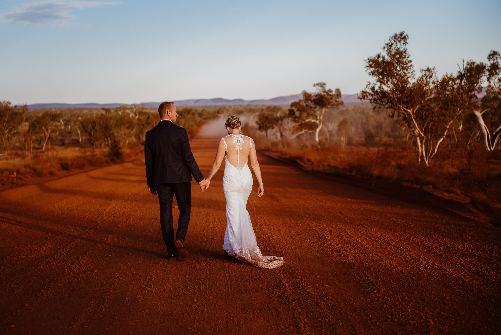 couple walking away from camera down red dirt road in Karijini on their wedding day
