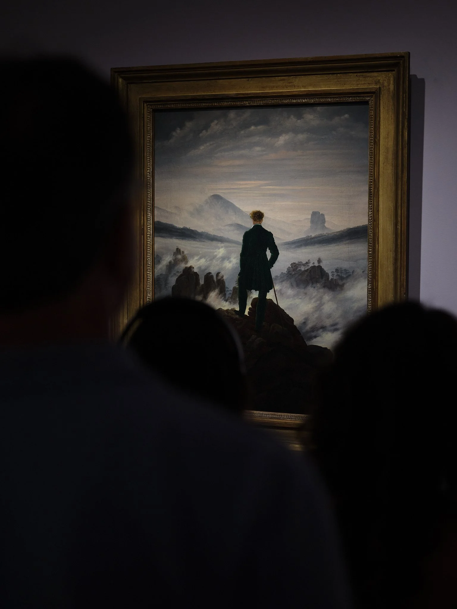 Photographed at The Metropolitan Museum of Art in New York. Visitors stand before Friedrich's Wanderer Above the Sea of Fog, becoming part of the image themselves—searching for what the painting depicts. The wanderer gazes toward an unreachable horiz