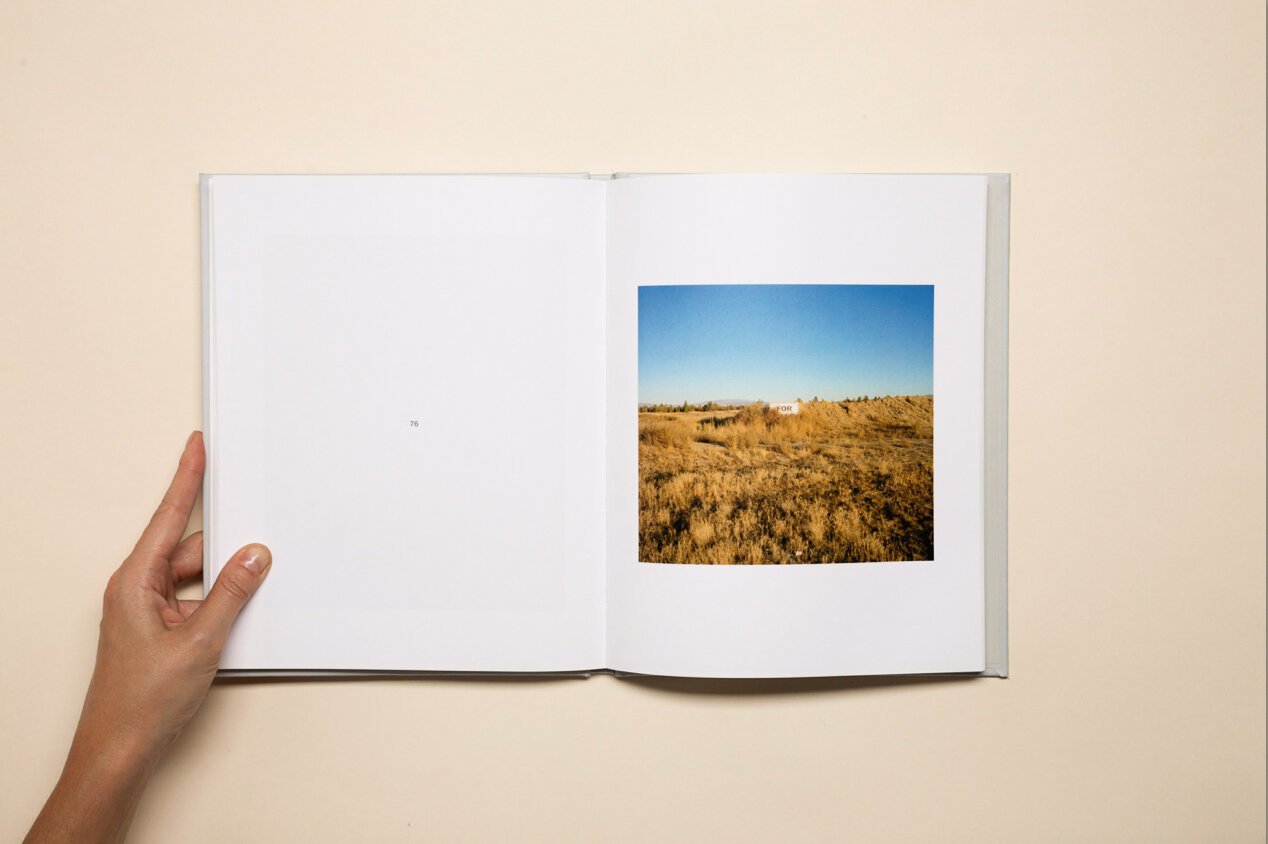 Open photo book showing a landscape with dry grass, shrubs, and a clear blue sky.