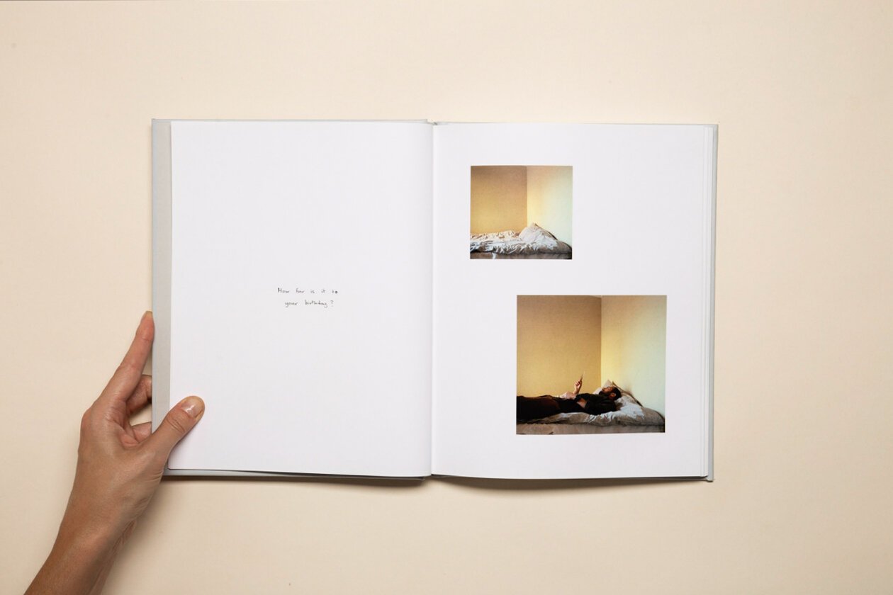 Open book with two photographs of a person lying on a bed against a plain yellow wall, with handwritten text on the left page reading 'How far is it to your bounding?'