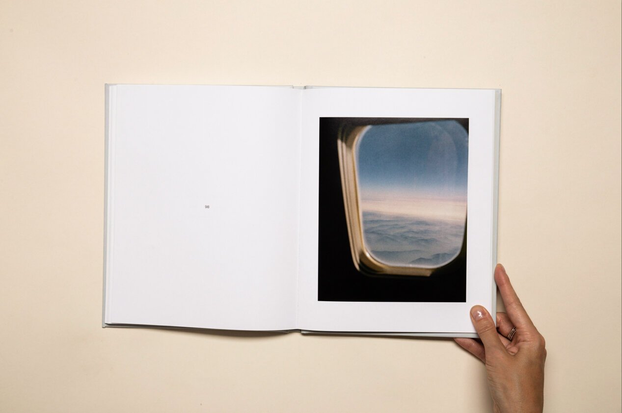 Open photo album showing a picture of an airplane window view with clouds and sky.