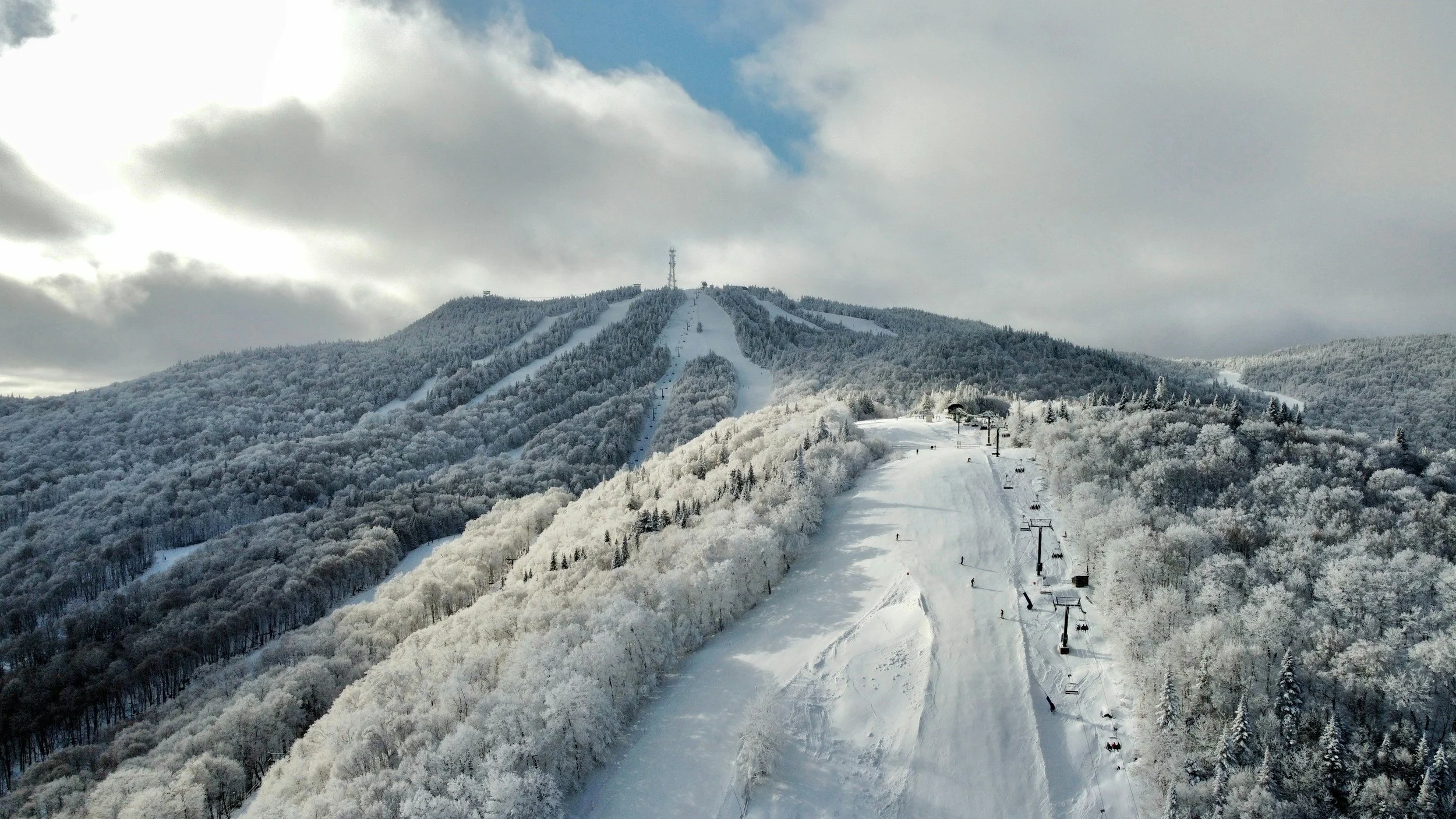 Aerial view of a snow-covered mountain ski resort with ski trails, chairlifts, and surrounding frosted trees.