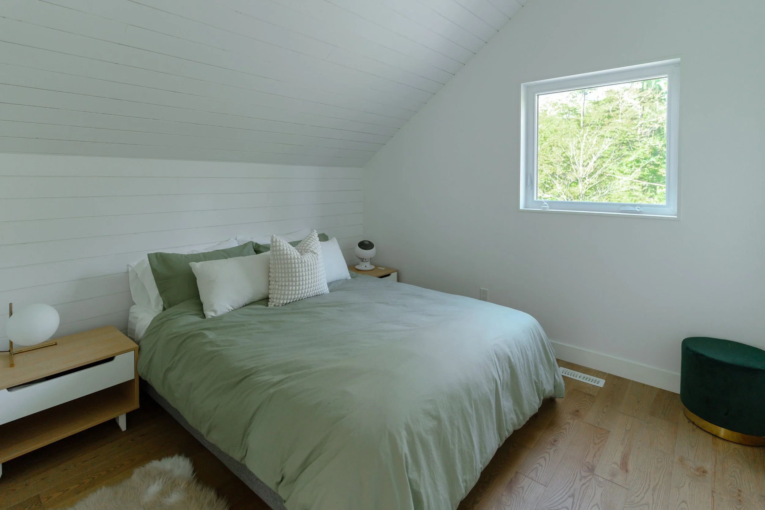 Minimalist bedroom with sloped ceiling, green bedding, and a window.