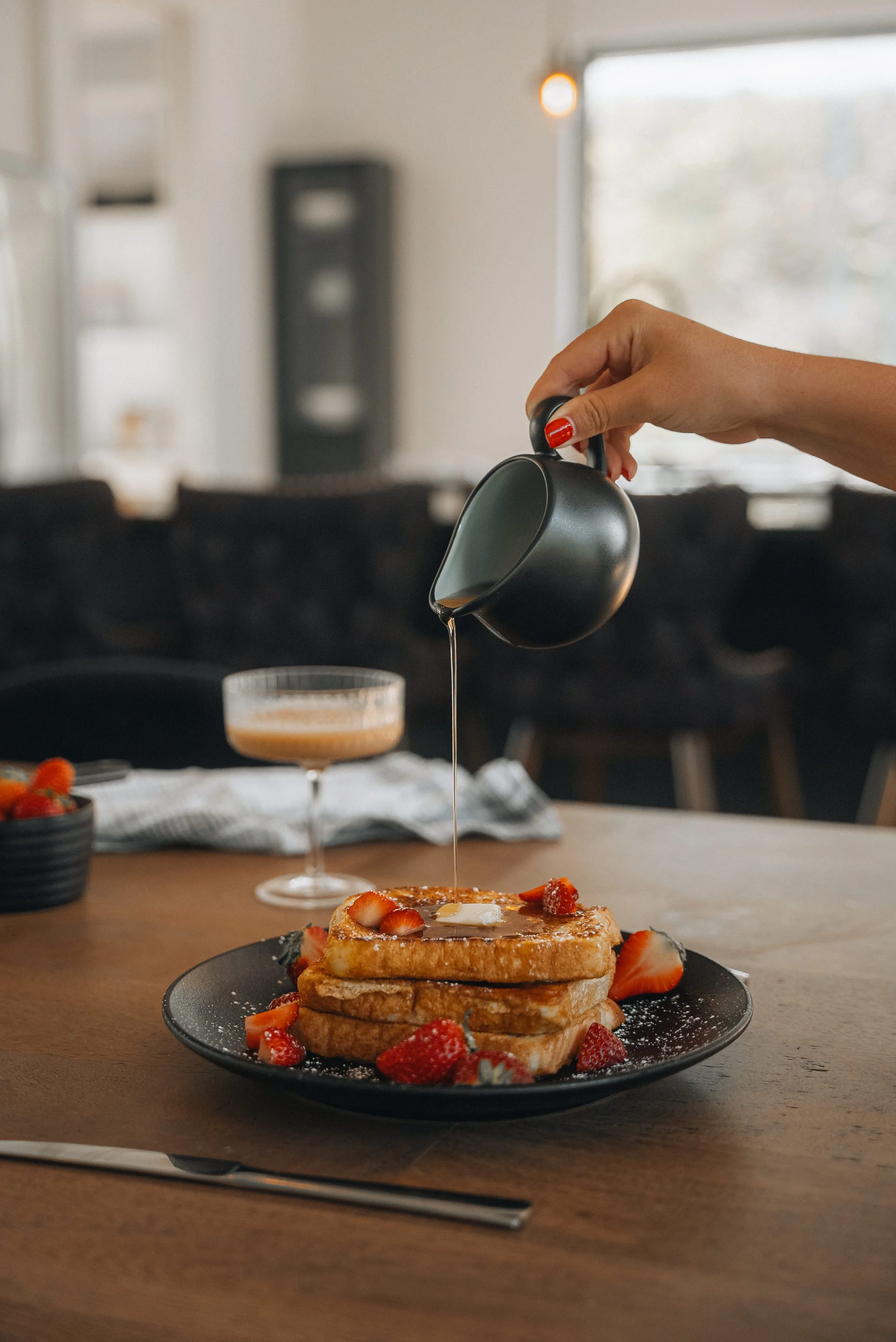 Person pouring syrup over French toast with strawberries.