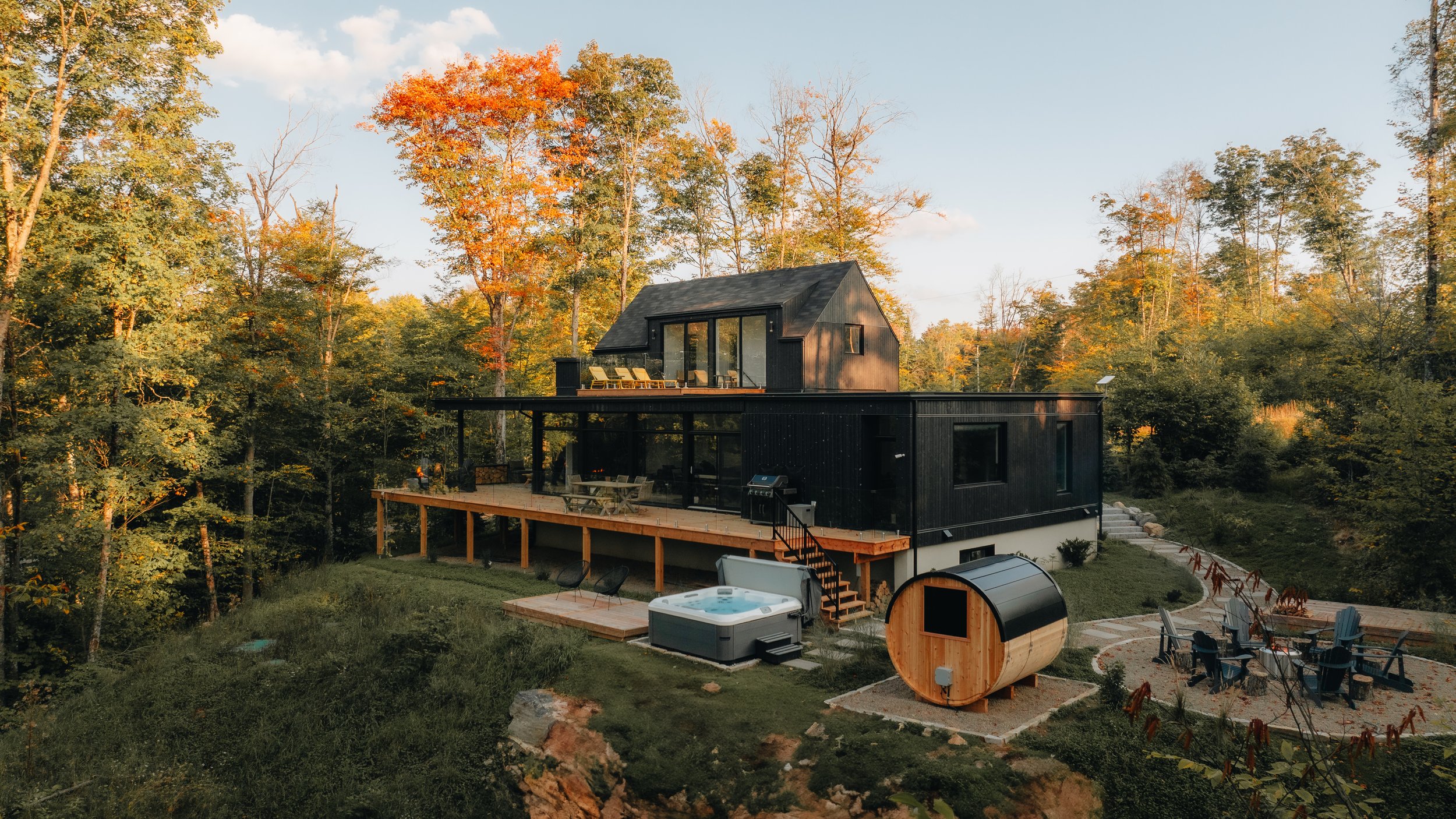 Modern cabin in a forest setting with a hot tub, sauna, and outdoor seating area.