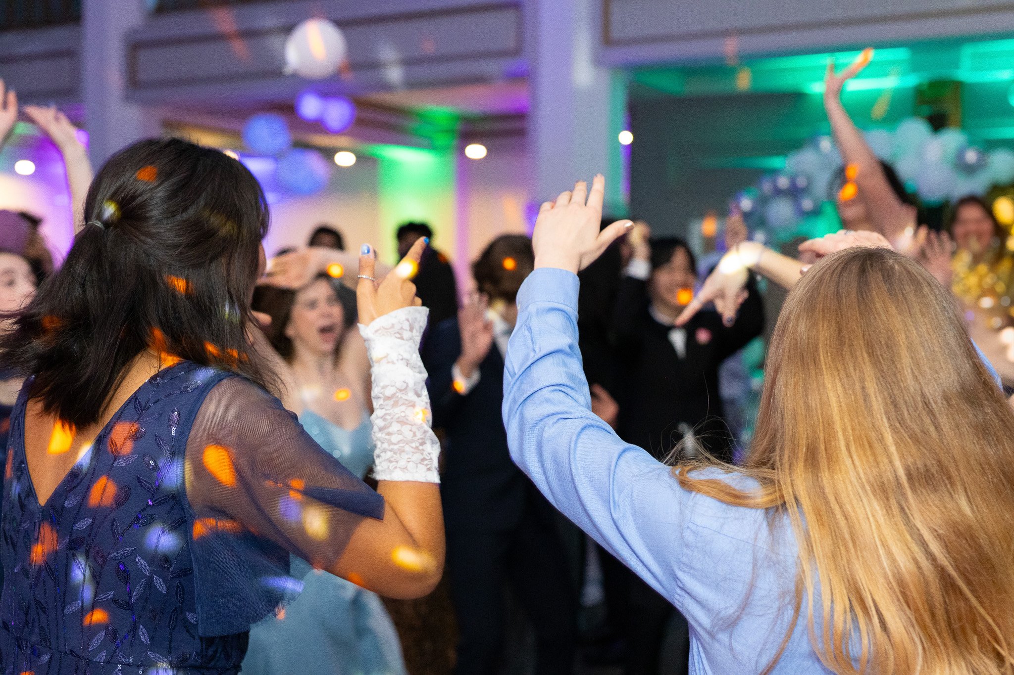 People dancing and socializing at an indoor party with colorful lighting and decorations.