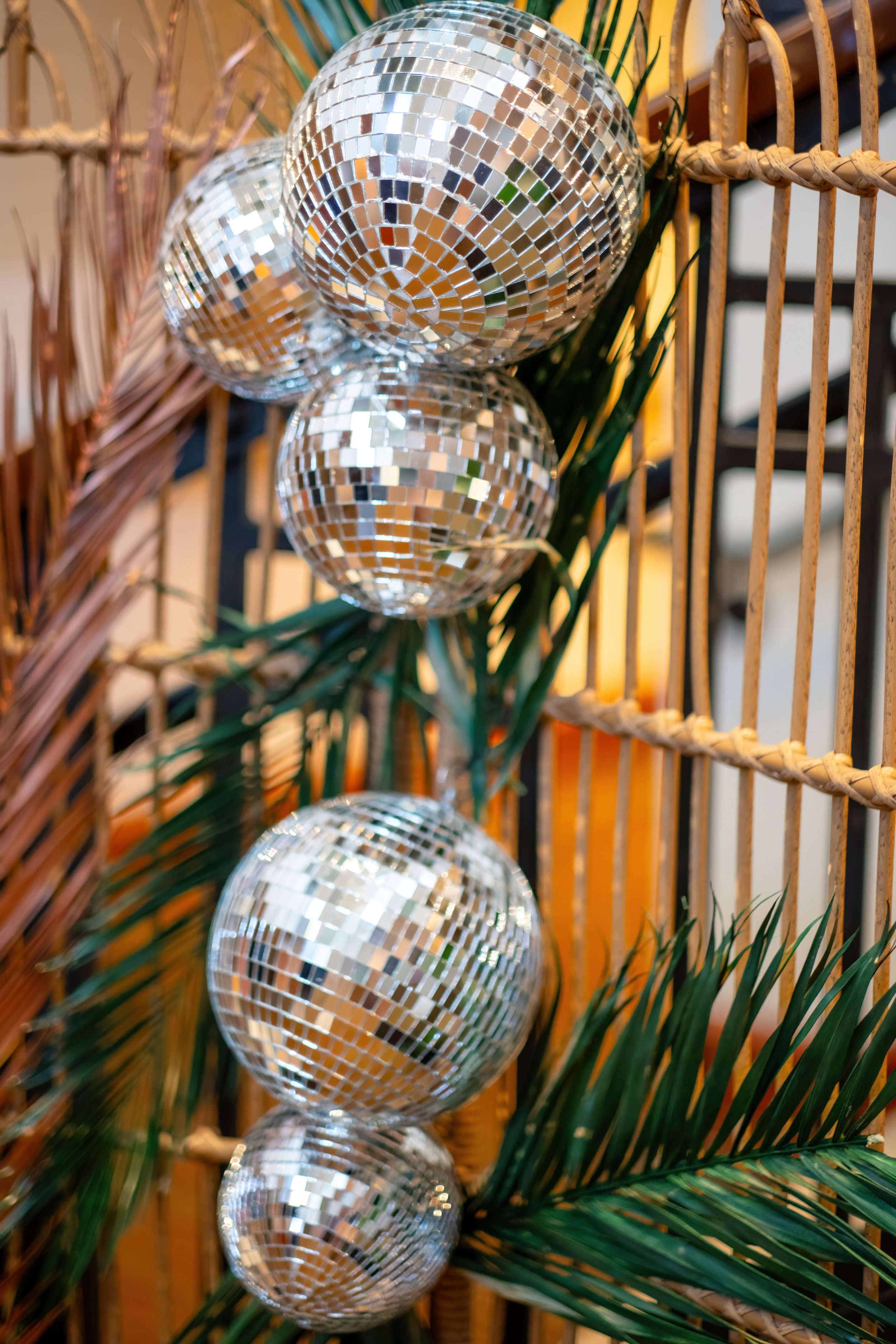 Four mirrored disco balls hanging with palm leaves on a bamboo frame, creating a festive display.