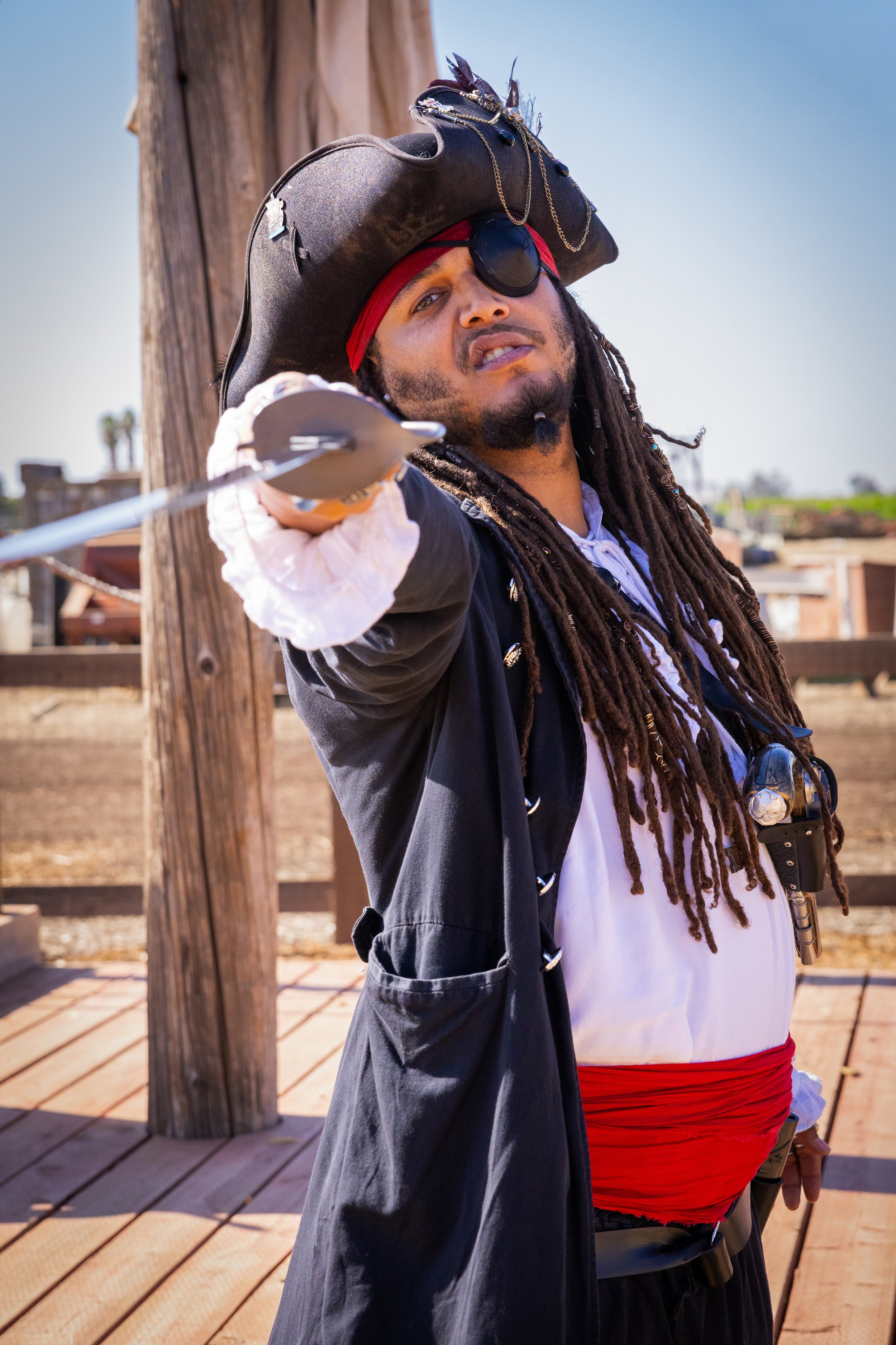 Person dressed as a pirate with a pirate hat, eyepatch, and costume pointing a sword towards the camera.