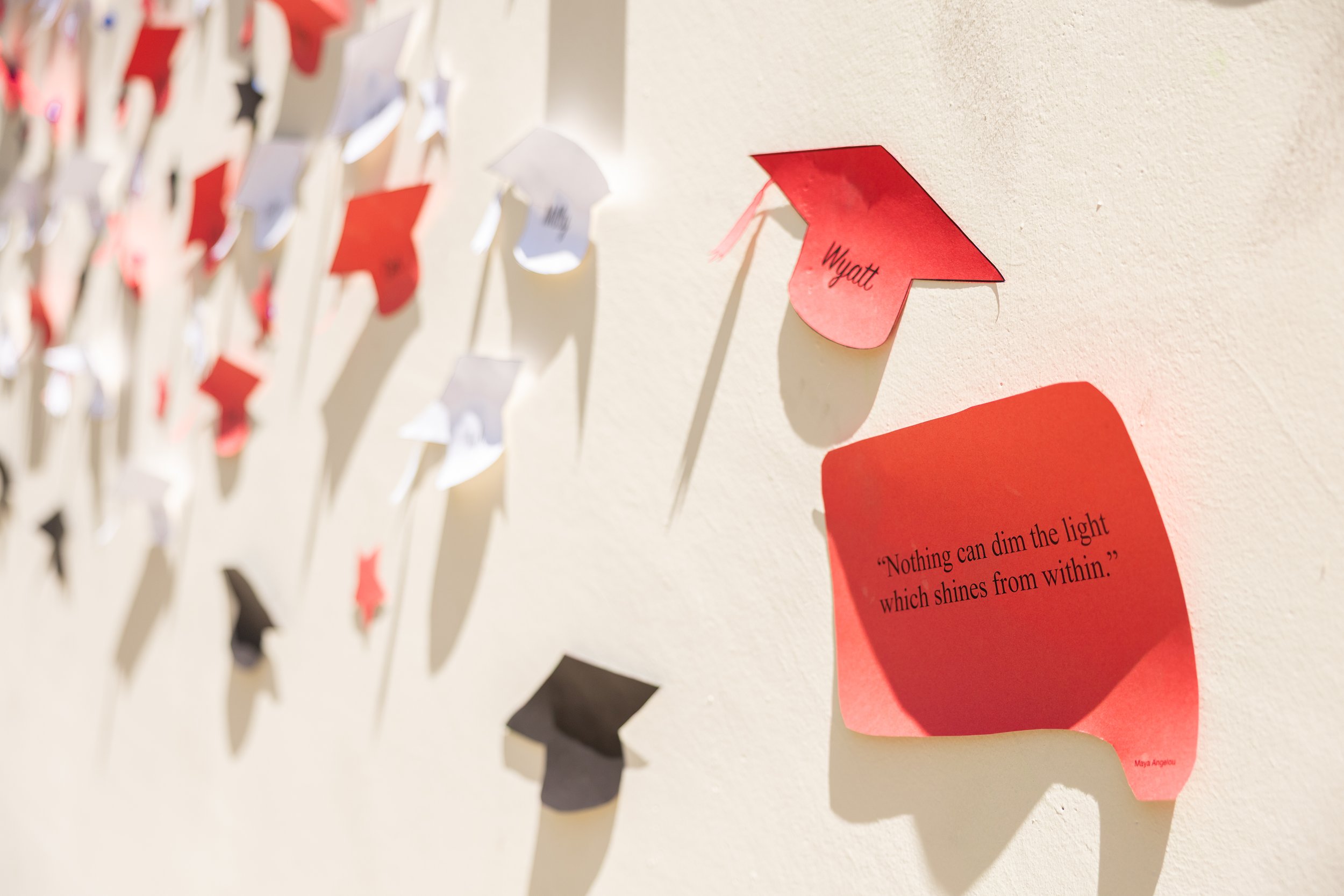 Wall decorated with red, white, and black paper graduation caps and a red paper reminder note with a quote.