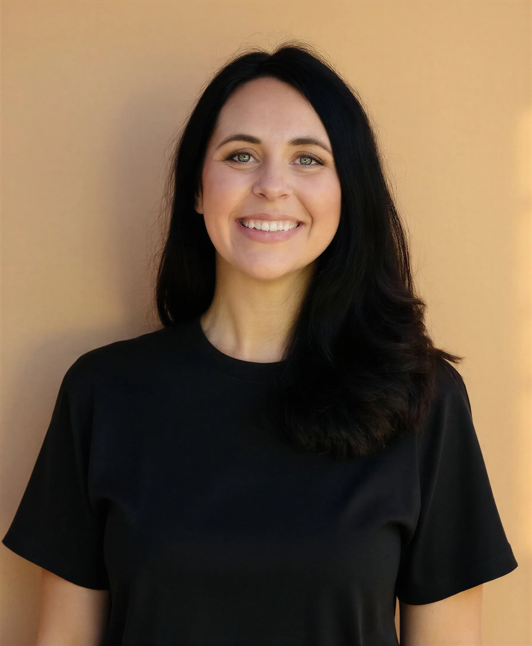 Close-up of a woman with long black hair, light eye color, and wearing a black shirt, smiling, against a beige background.