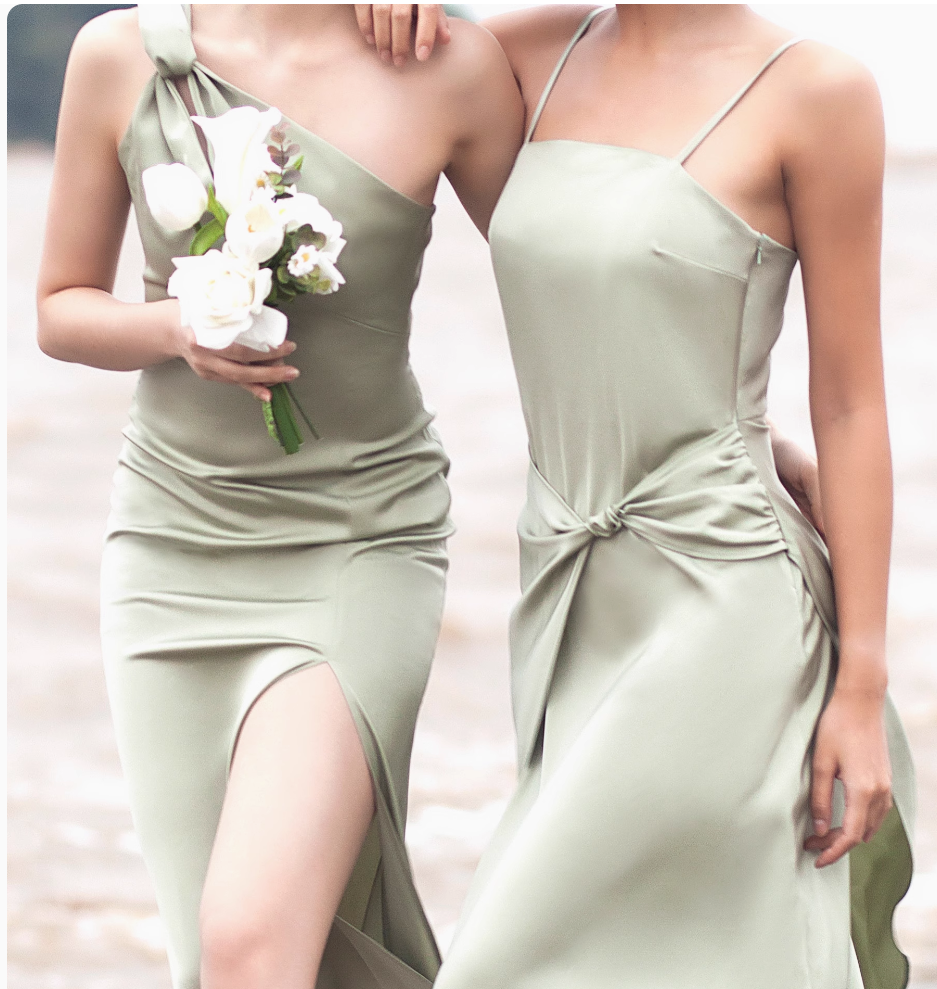 Two women in light green dresses walking, one holding a bouquet of white flowers.