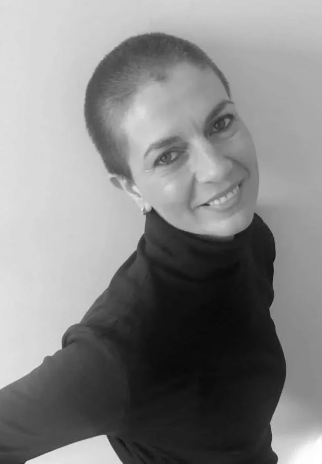 A woman with a short buzz haircut wearing a black turtleneck, smiling at the camera, in black and white.