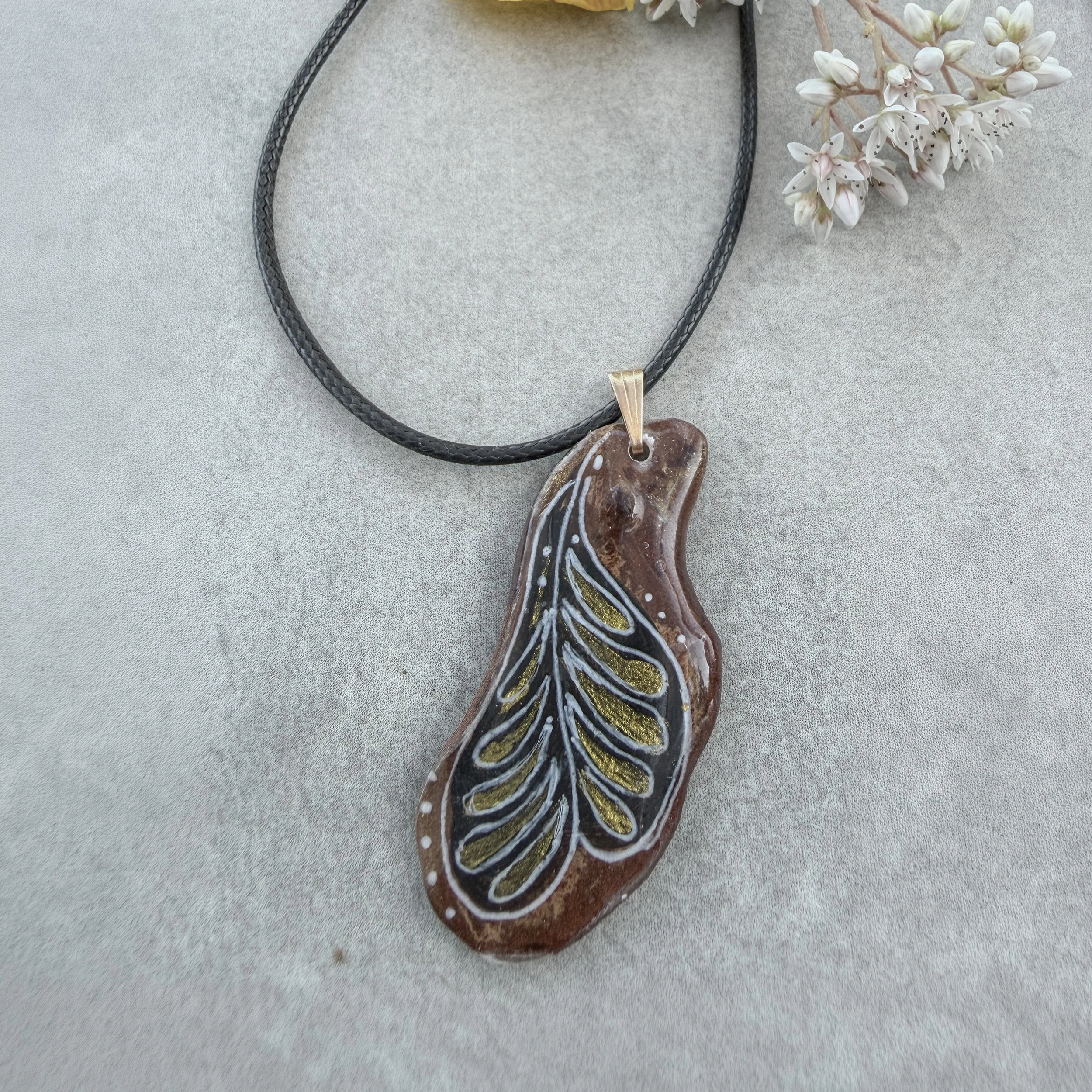 Hand-painted bark jewellery pendant 'Plume' — single feather motif in gold and white on deep black reclaimed bark, waxed leather cord