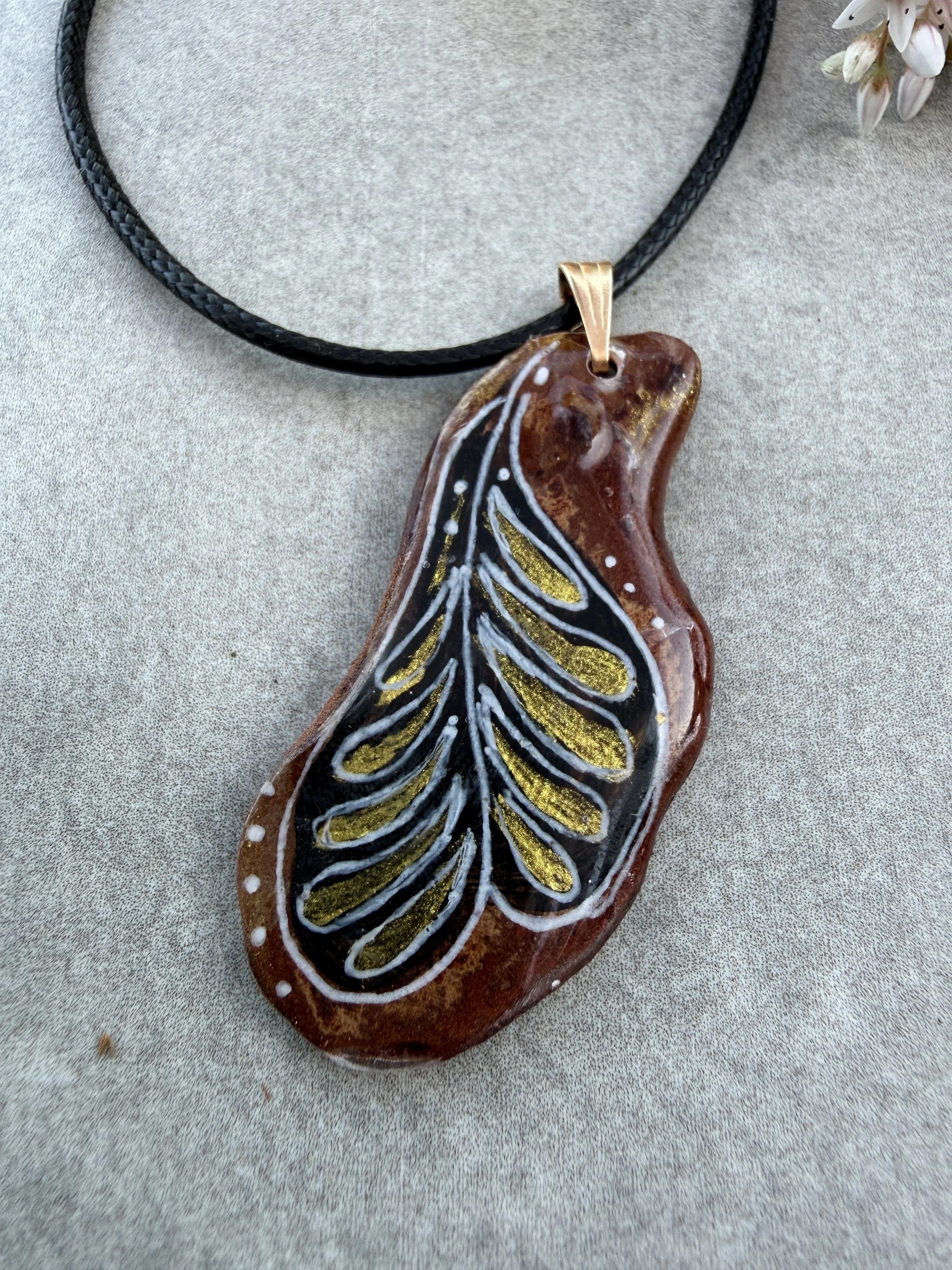 Close-up of 'Plume' bark pendant — gold and white hand-painted plume motif on deep black Crimean pine bark, one-of-a-kind wearable art