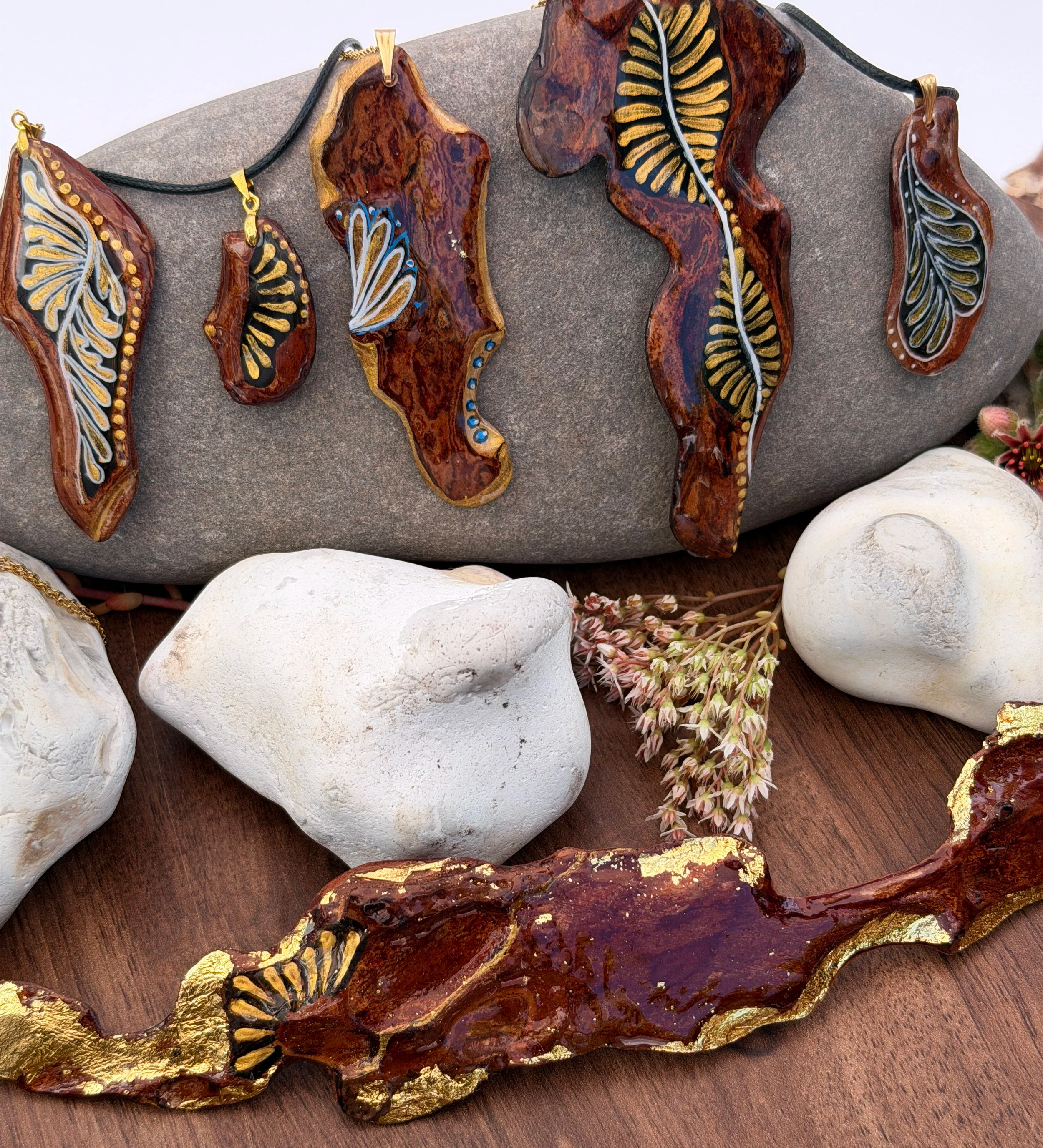 Hand-painted bark jewellery collection by Roxy Megyesi — one-of-a-kind bark pendants with gold and botanical motifs, displayed on natural stones, Bark & Grain Studio Bristol