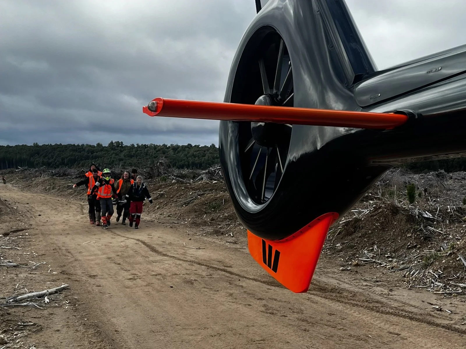 Rescue team walking on a dirt trail near a crashed aircraft with a large wheel and orange rescue equipment.