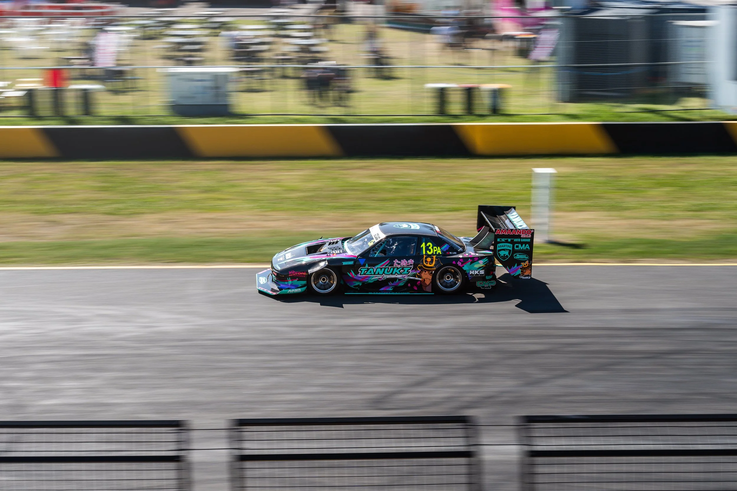 Race car speeding on track with colorful graphics and sponsor logos, blurred background indicating motion.