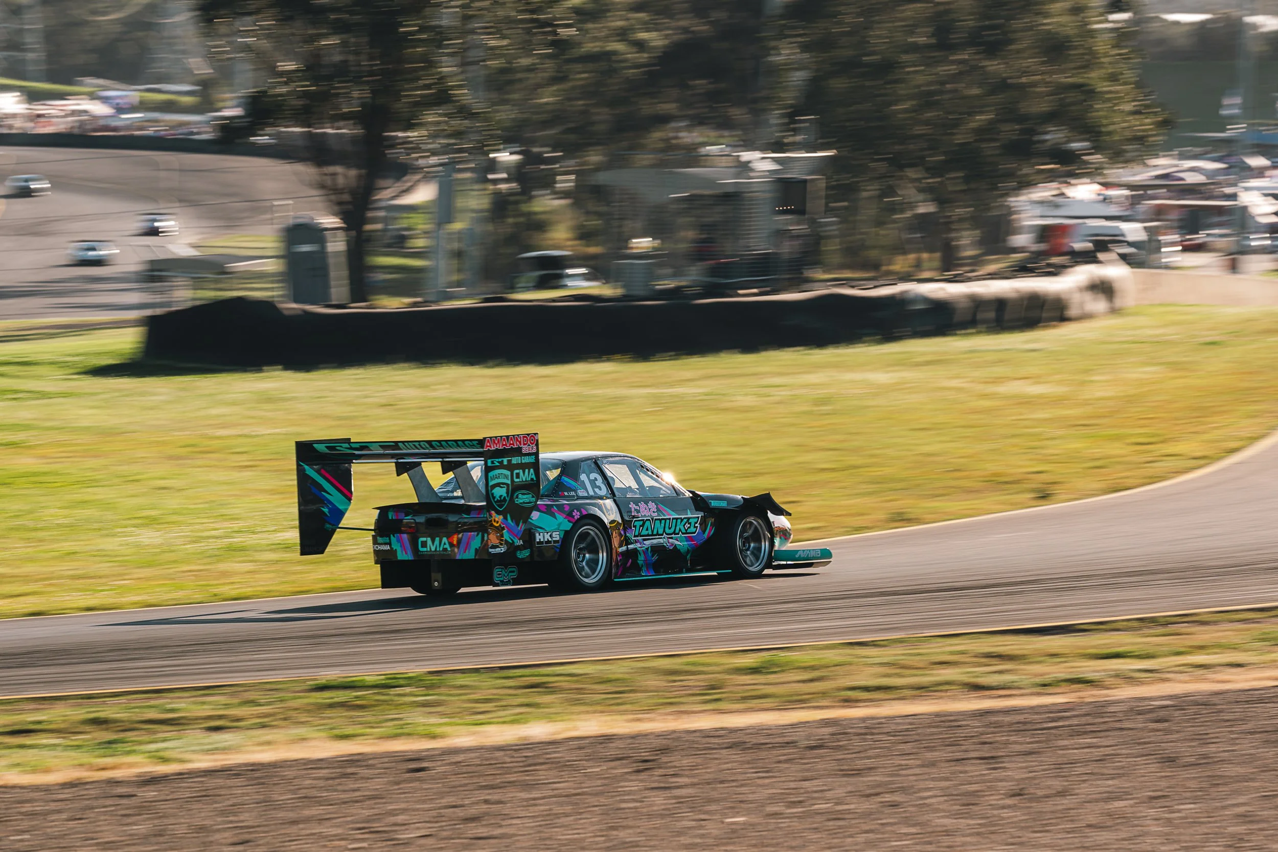 A race car driving on a race track during daytime, with a grassy field and trees in the background.