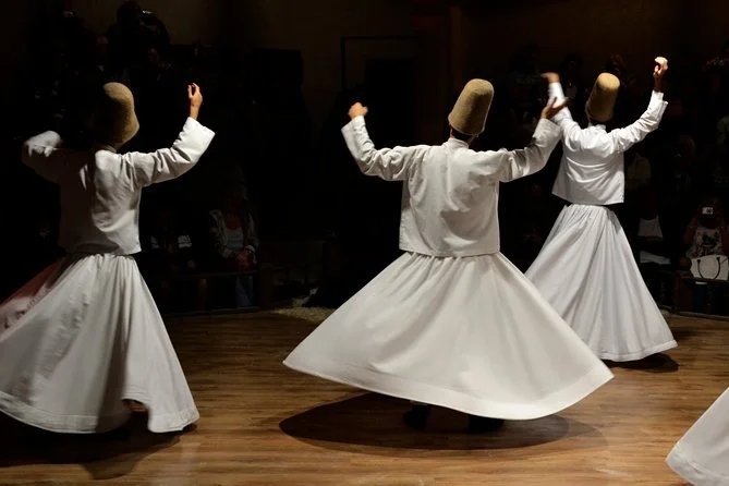 A mesmerizing moment from the Cappadocia Dervish Show, featuring whirling dervishes in flowing white robes spinning gracefully in a spiritual dance. The dimly lit setting enhances the sacred and serene atmosphere, with the performers moving in perfec