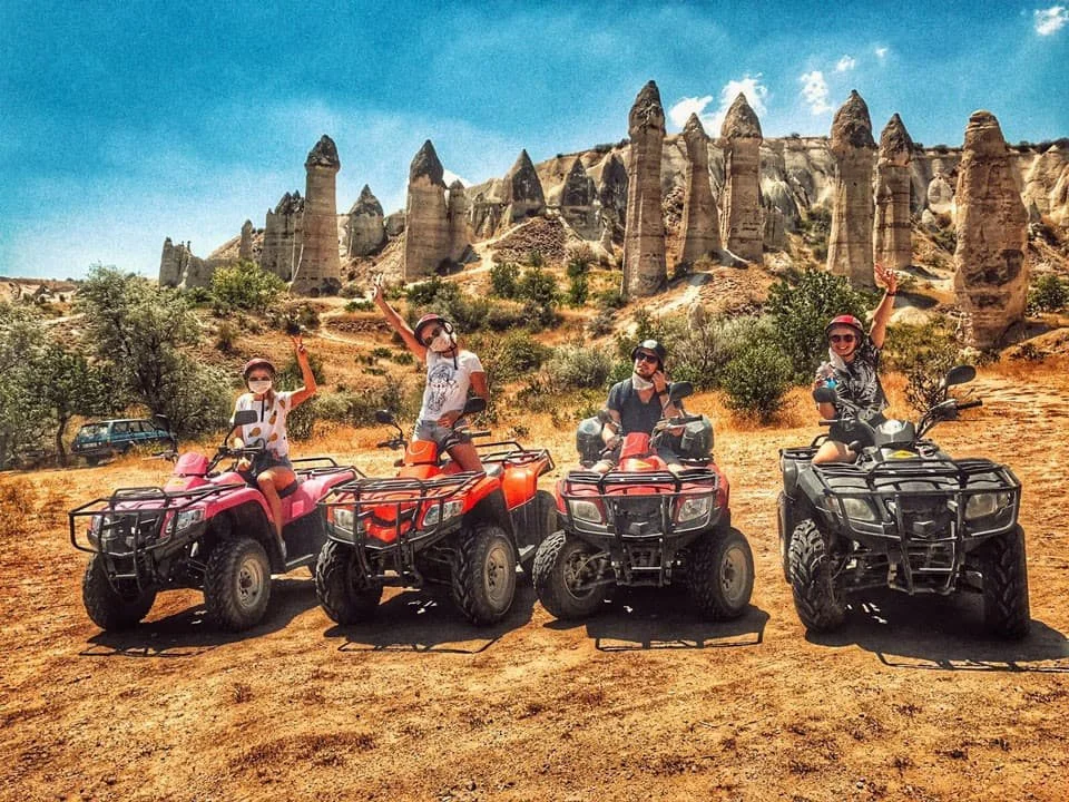 Rider on an ATV navigating through the dusty trails and valleys of Cappadocia, with unique rock formations and fairy chimneys in the background during a thrilling sunset adventure.