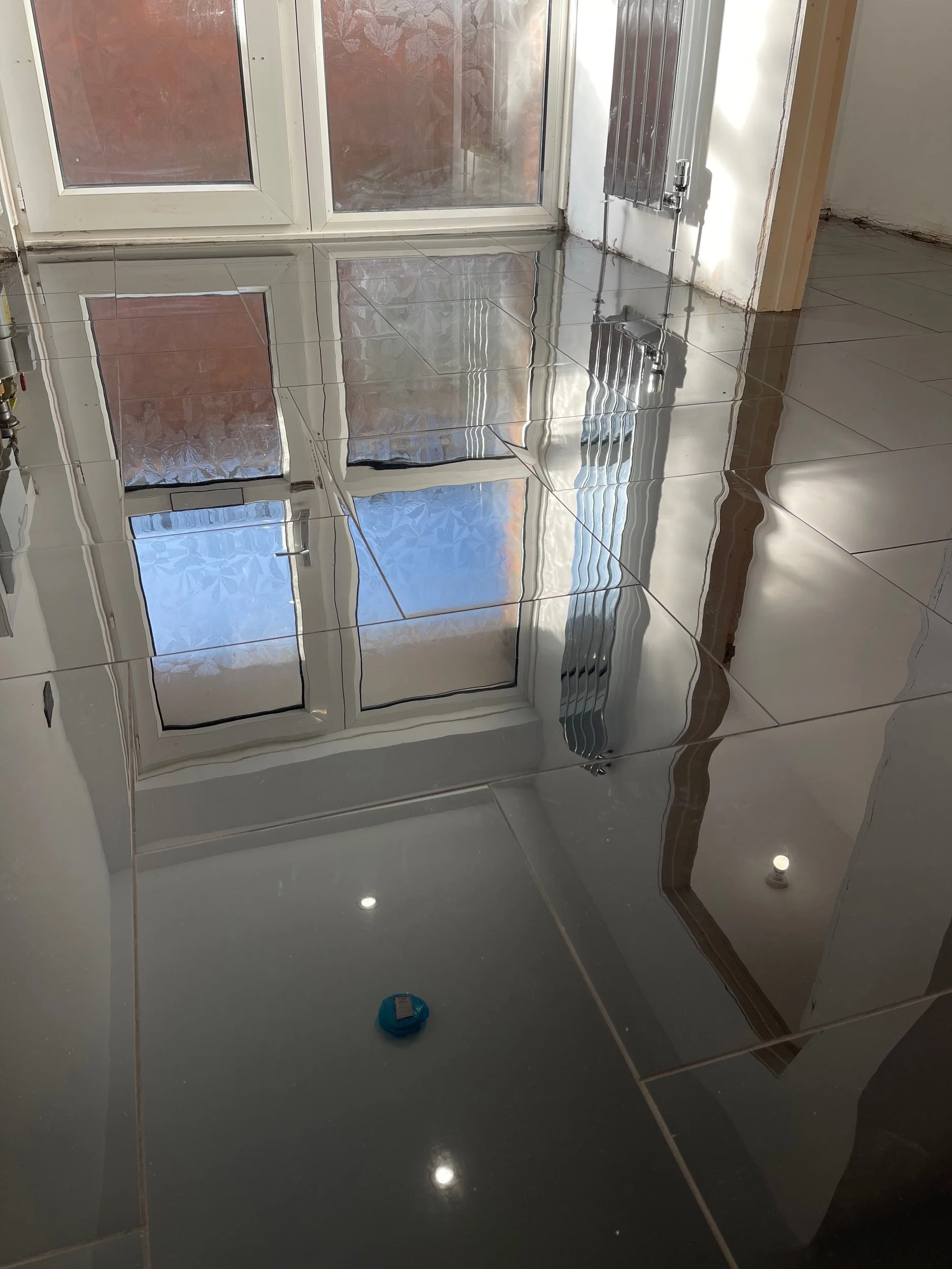 Room with shiny, reflective tiled floor, white walls, large window with frosted glass, and a radiator underneath the window.