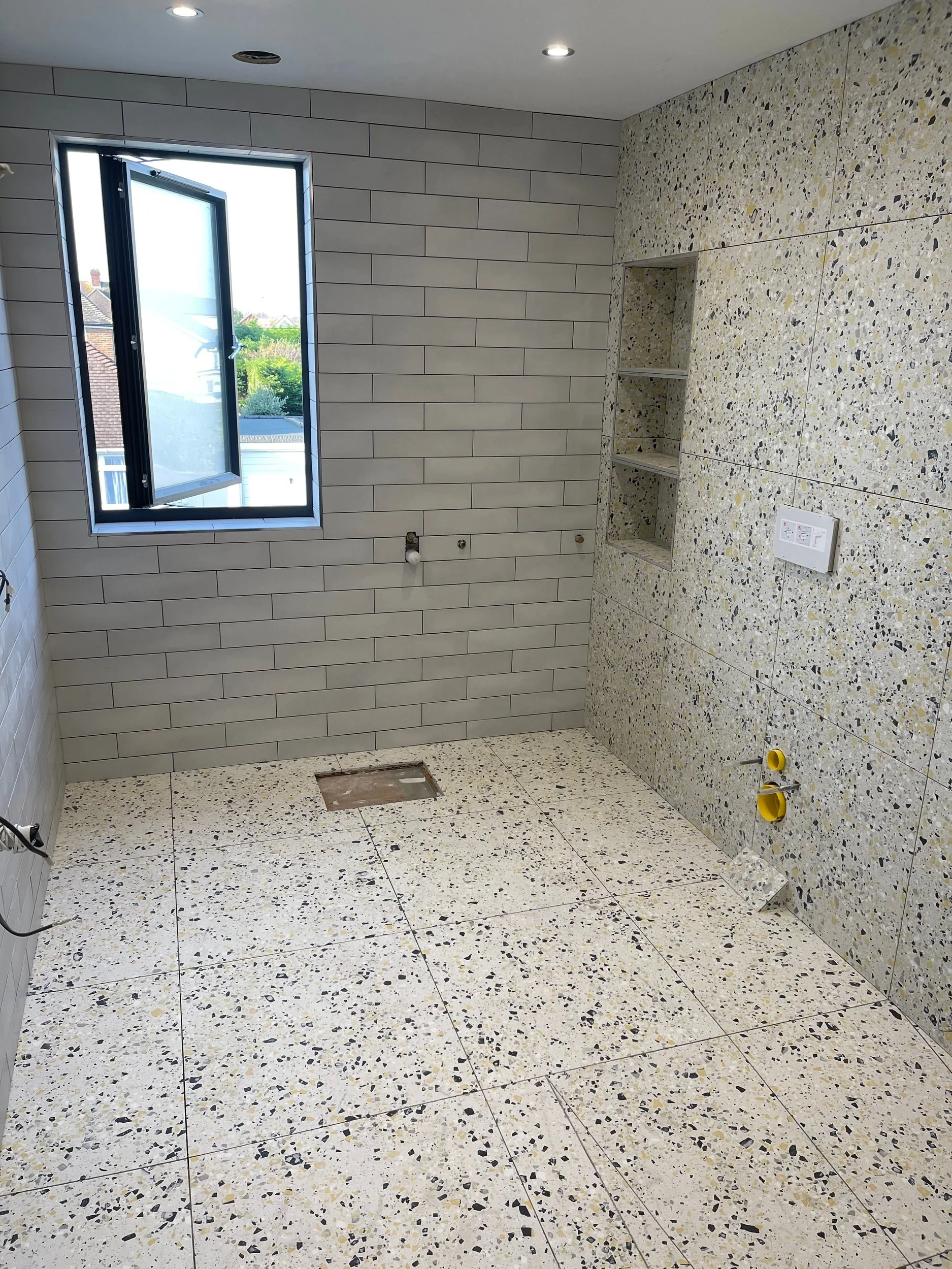 Empty room under construction with tiled walls and floors, an open window, and electrical outlets.