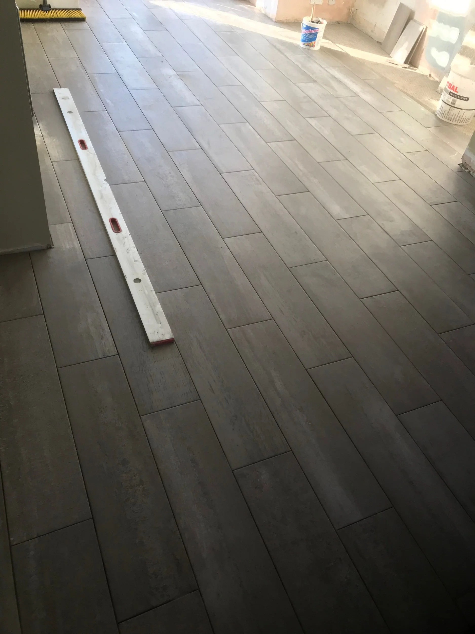 Newly installed gray wood-look ceramic tile flooring in a room under construction, with construction tools and supplies visible.