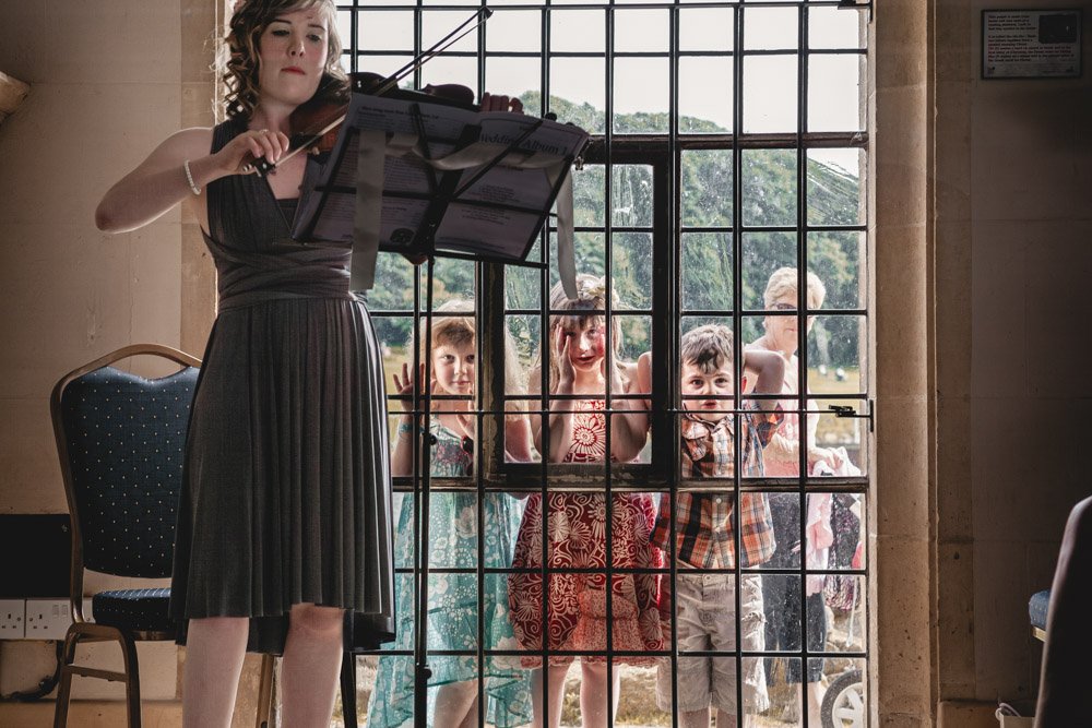 children peer through church window as violinist performs a song