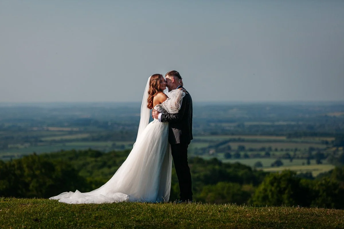 bride and groom kiss on top of dovers hill in the cotswolds