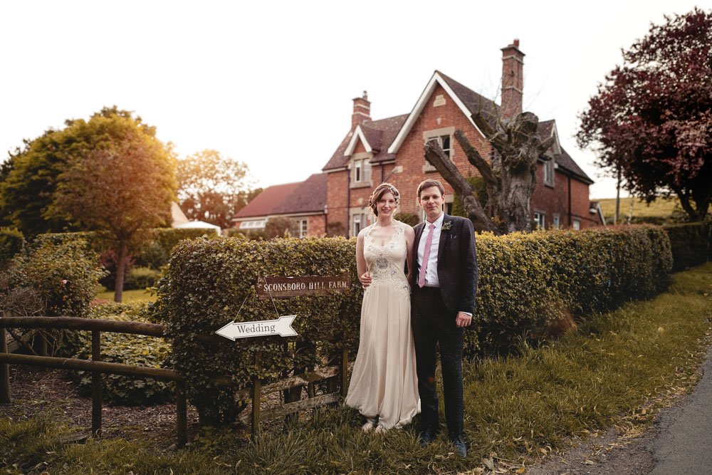 bride and groom stand in front of family farmhouse