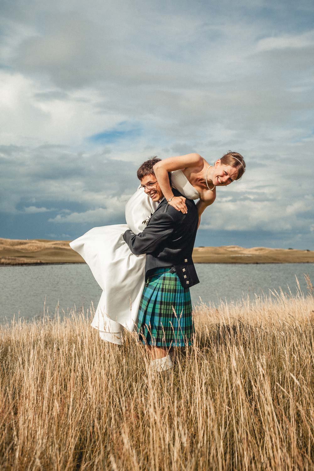 groom lifts bride on shoulder in grassy Oxfordshire meadow