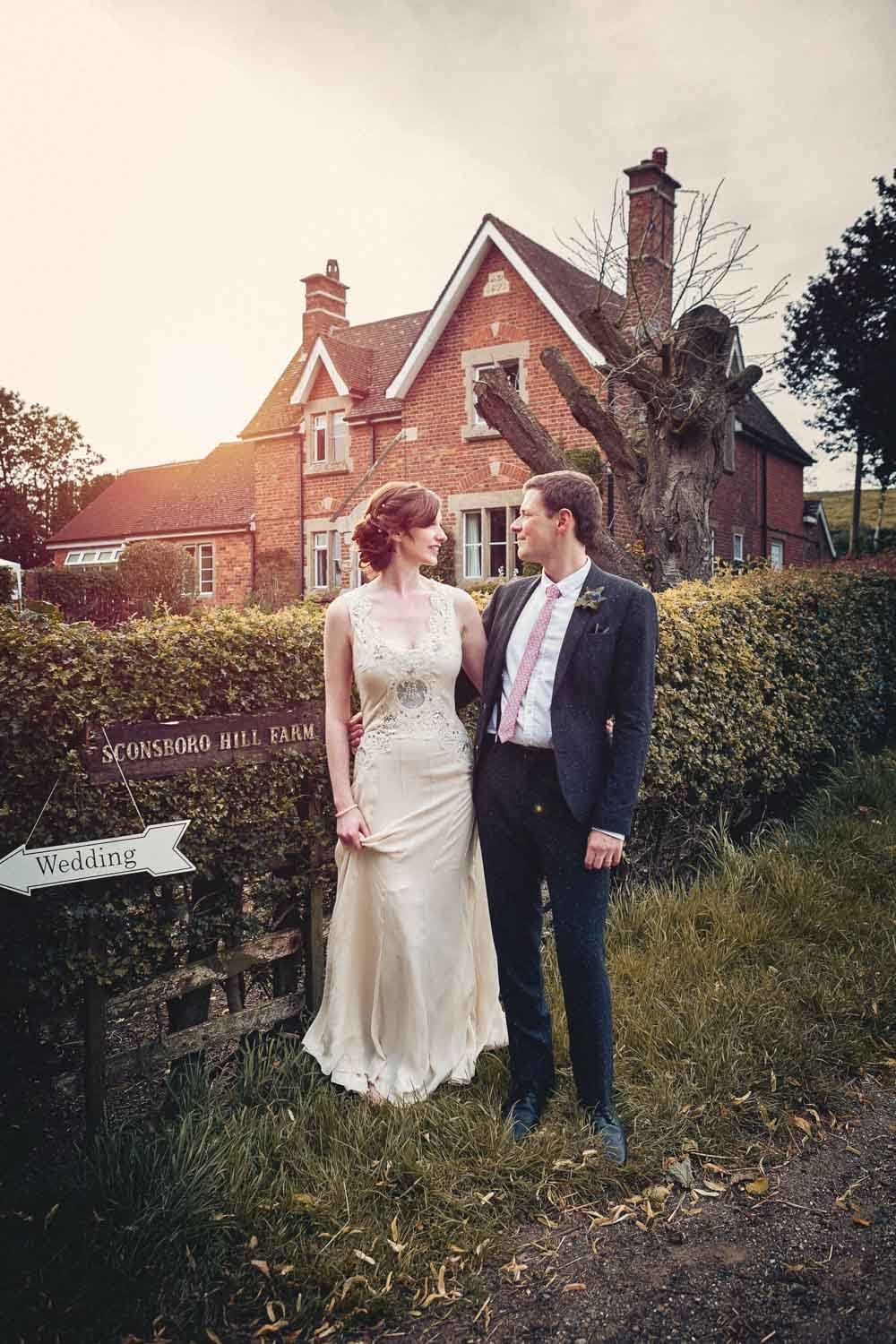 bride and groom stand in front of family farm house