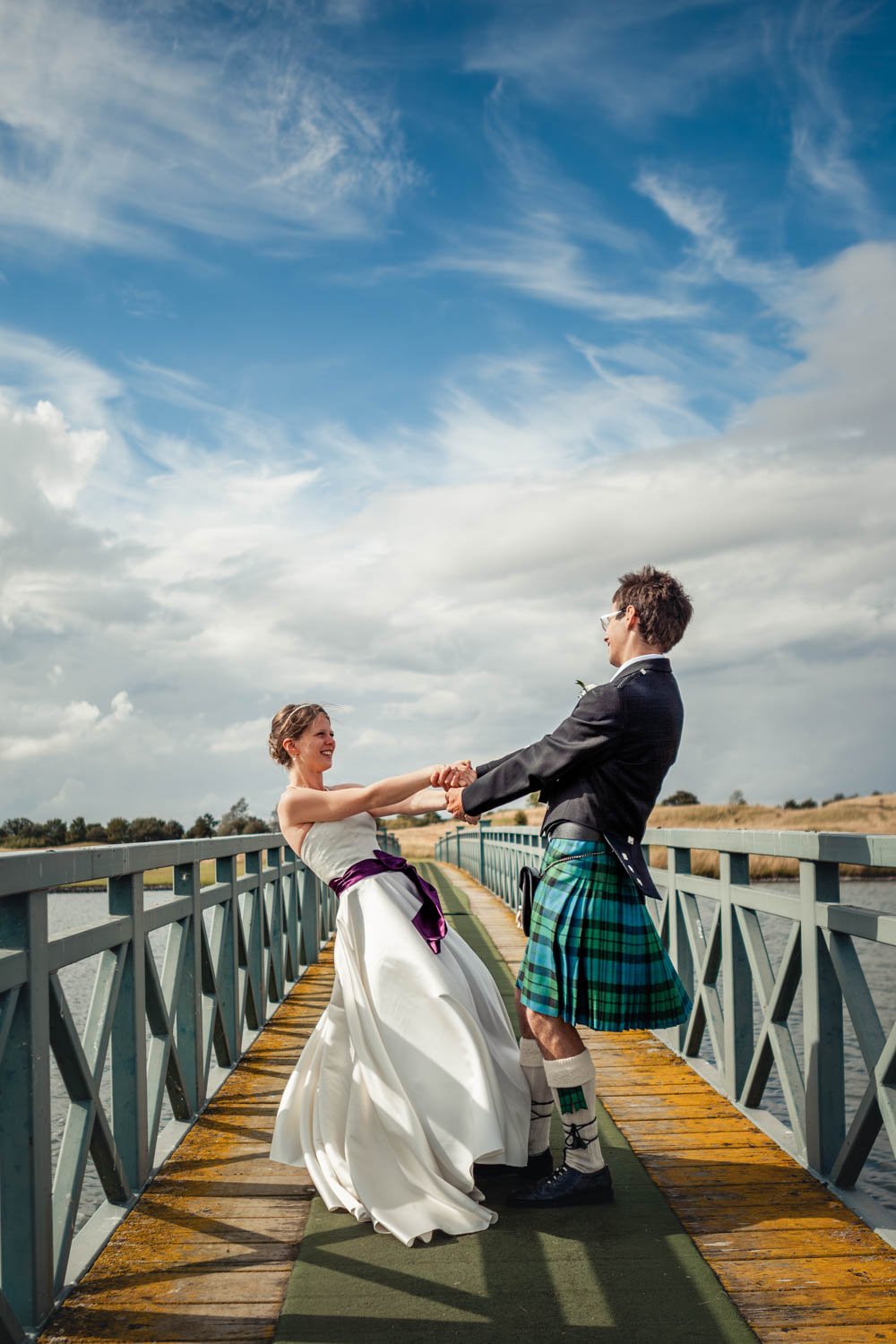 bride and groom spin around on a bridge