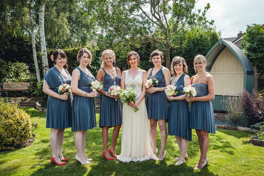 bride and bridesmaids in grey dresses pose in the garden