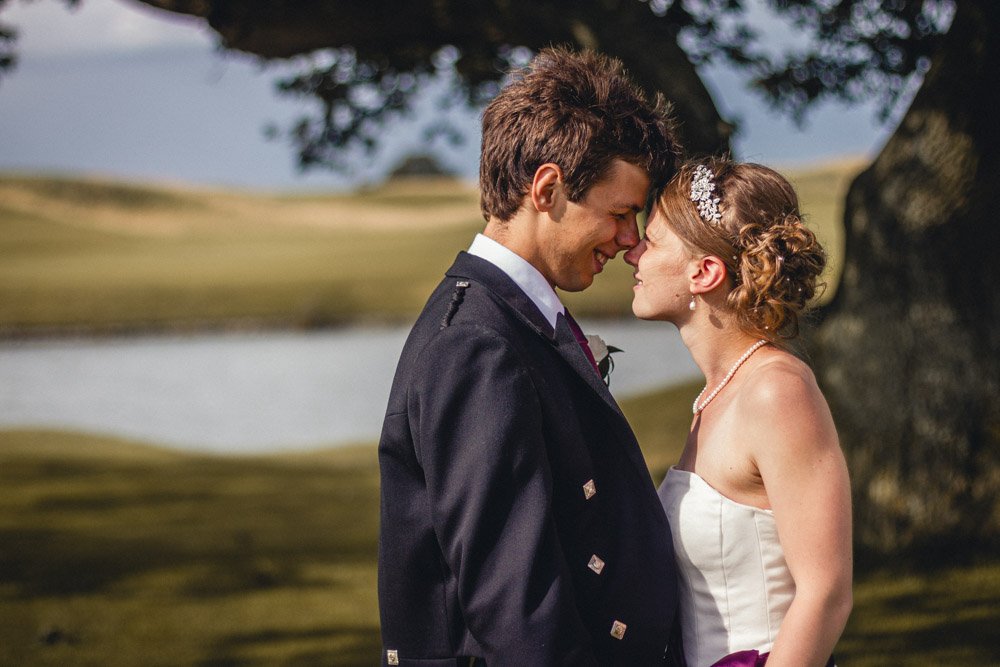 bride and groom bump noses by lake on Oxfordshire gold course