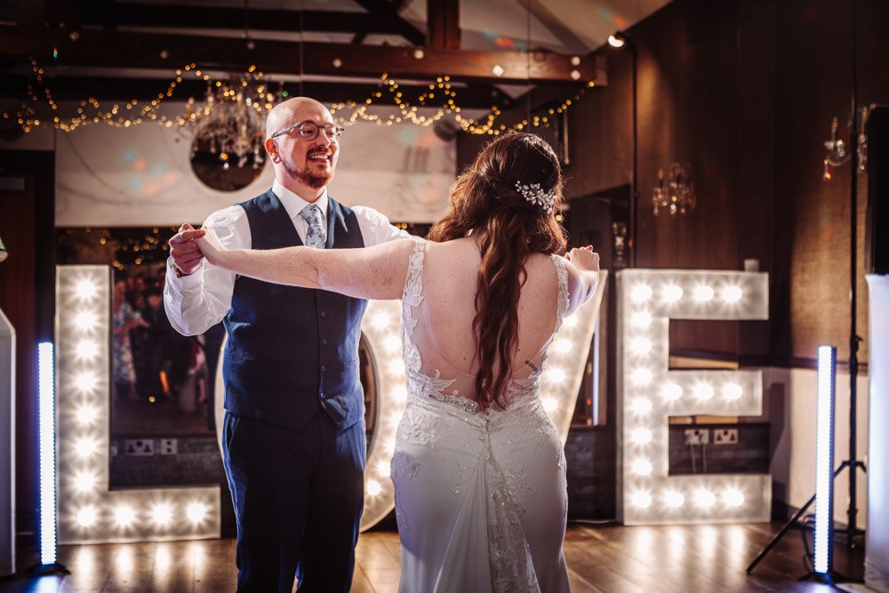 bride and groom first dance in front of light-up LOVE letters